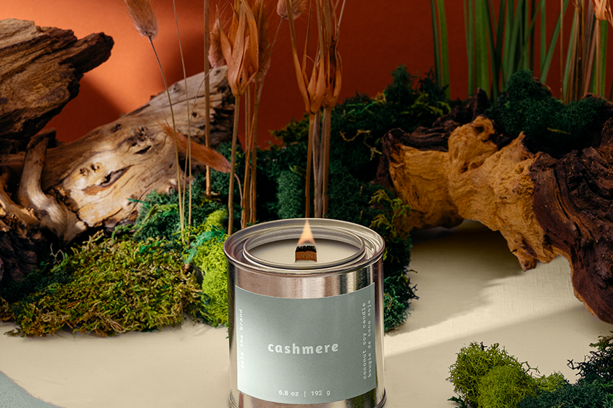 Candle labeled 'cashmere' in a natural setting with plants and wood.