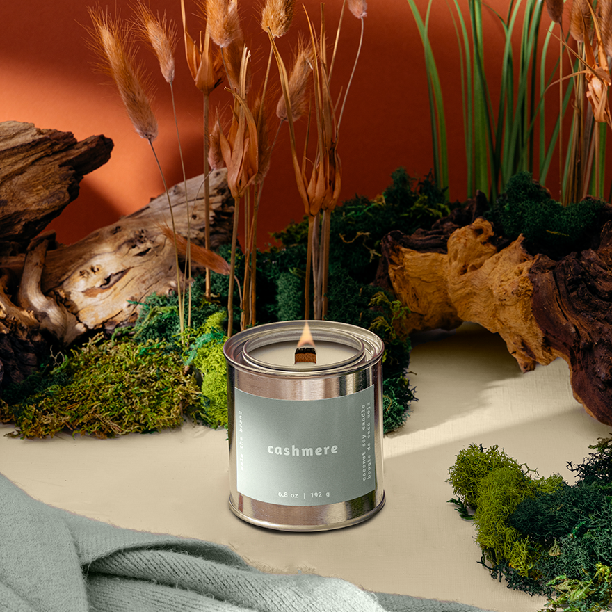 Candle labeled 'cashmere' in a natural setting with plants and wood.