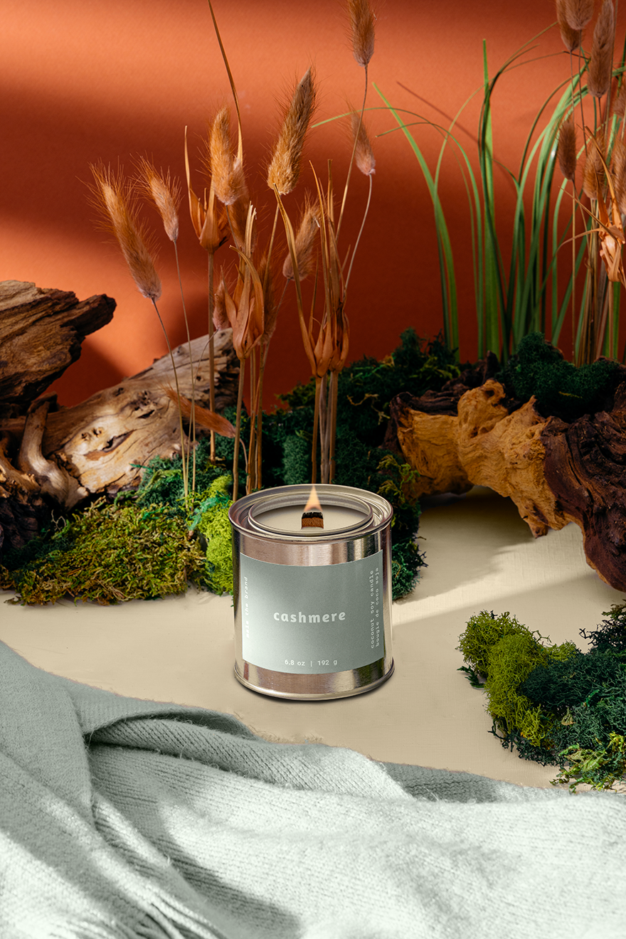 Candle labeled 'cashmere' in a natural setting with plants and wood.