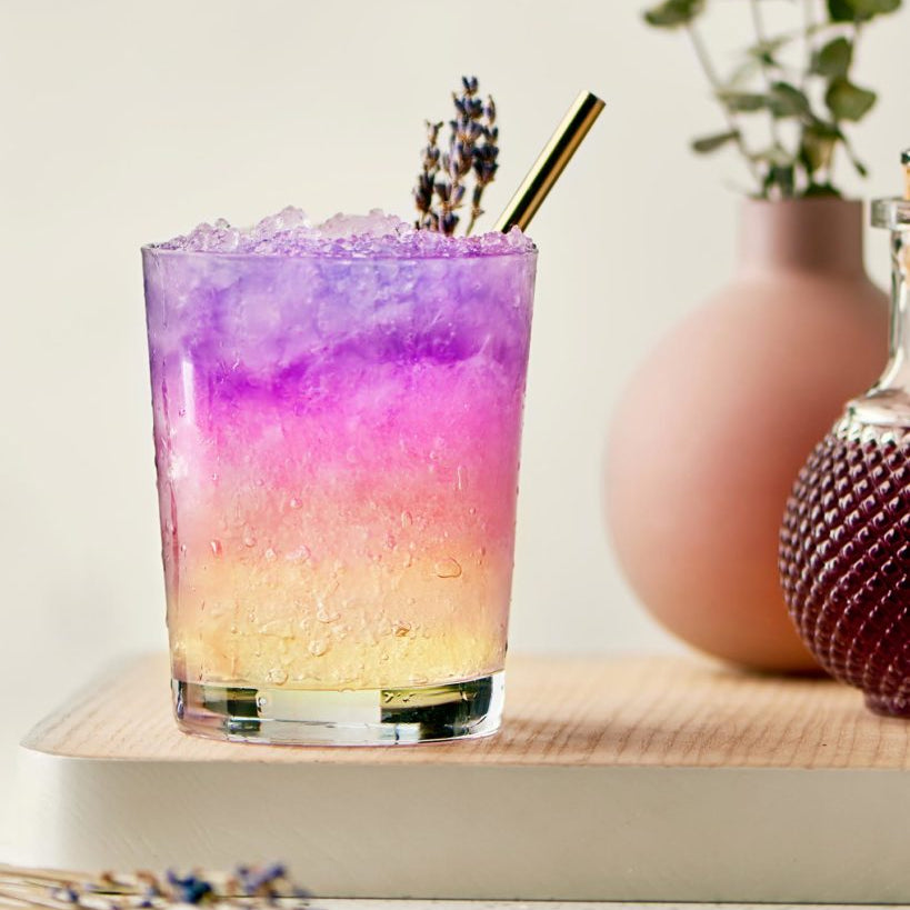 Colorful cocktail with ice and lavender garnish on a wooden surface with a light background The Sobr Market