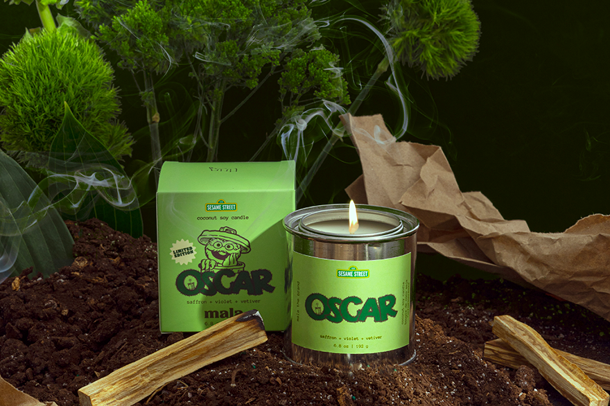 Candle labeled 'Oscar' with a green label on a dark background with plants.