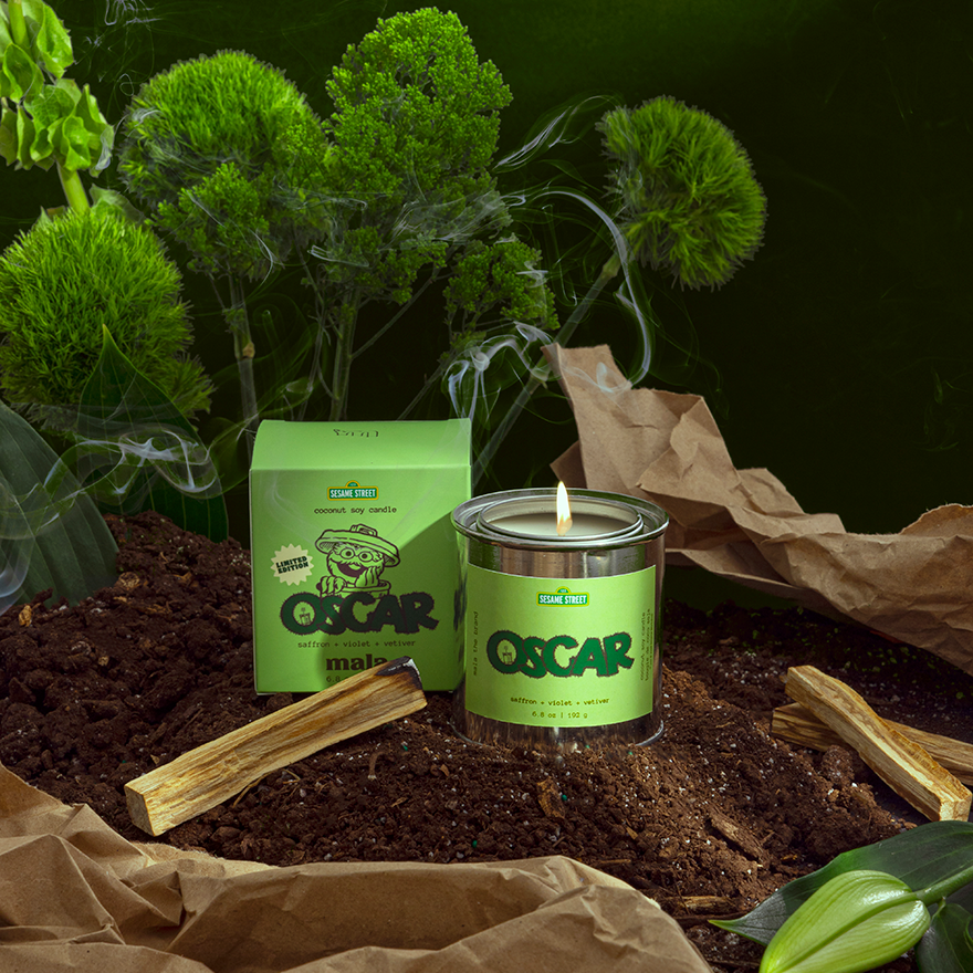 Candle labeled 'Oscar' with a green label on a dark background with plants.