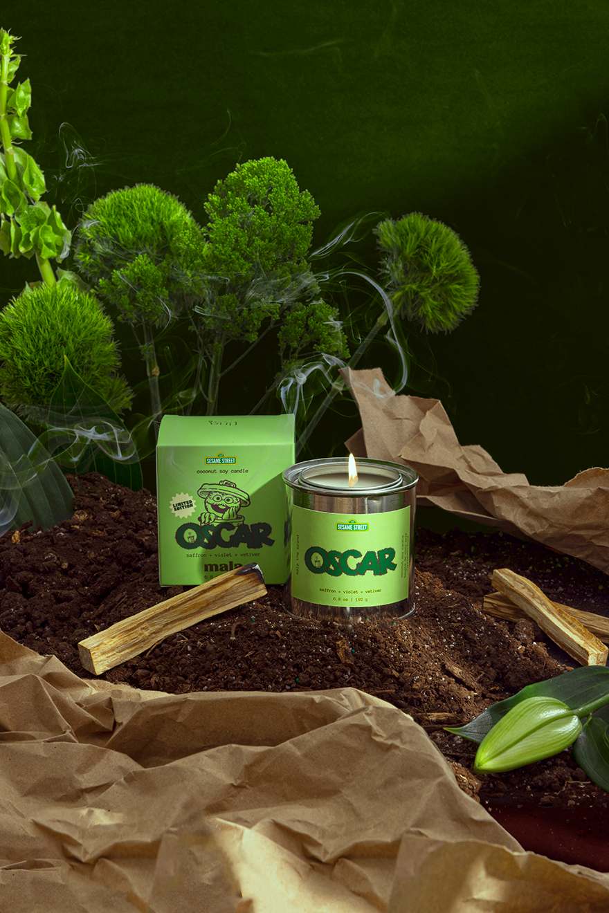 Candle labeled 'Oscar' with a green label on a dark background with plants.