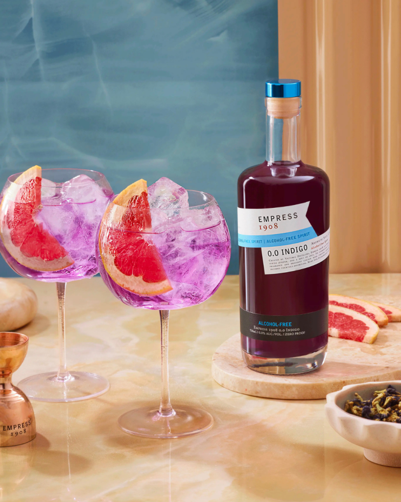 Bottle of Empress 1908 alcohol-free gin with two pink cocktails and grapefruit slices on a table. The Sobr Market