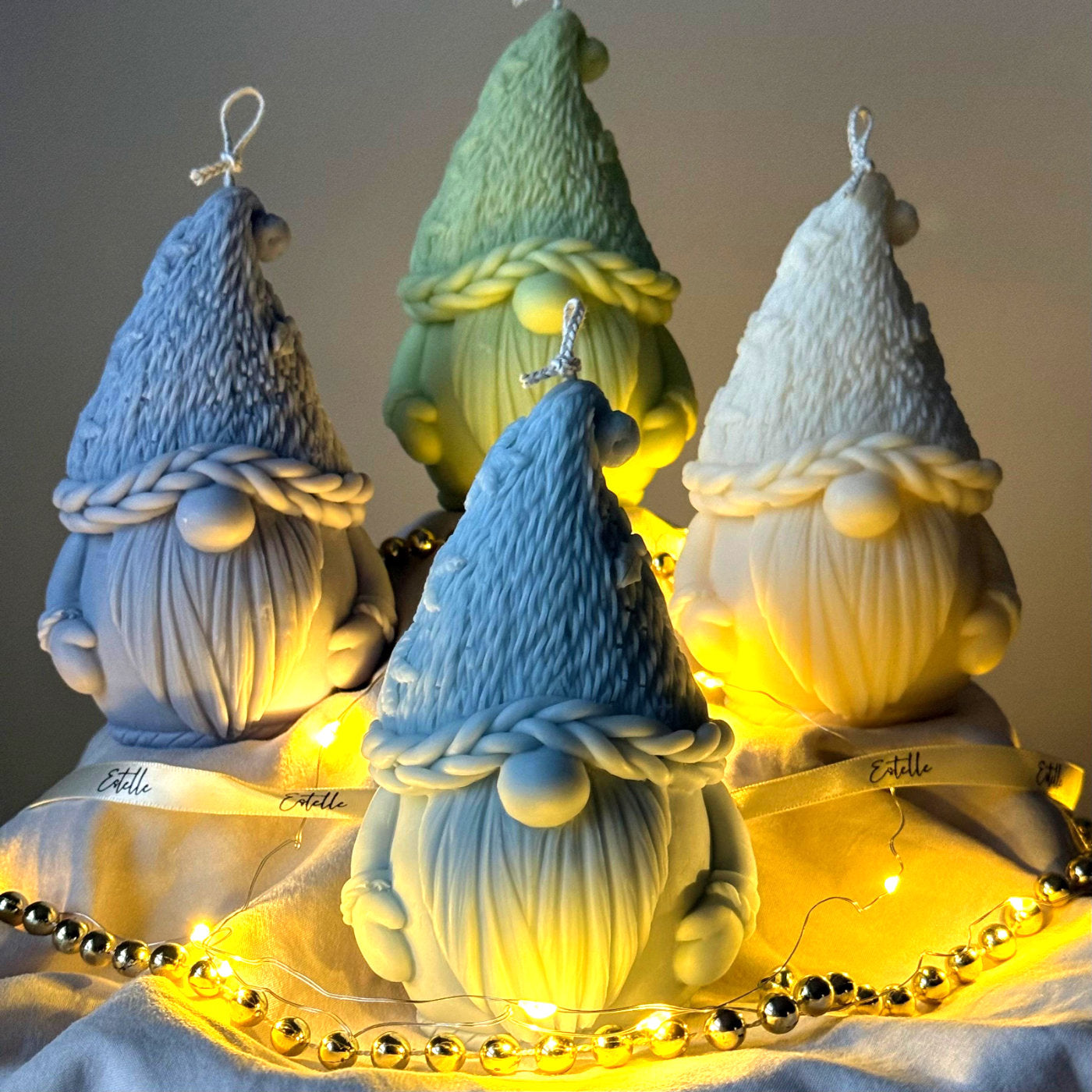 Four colorful Gnome-shaped candles on a wooden stand with string lights.