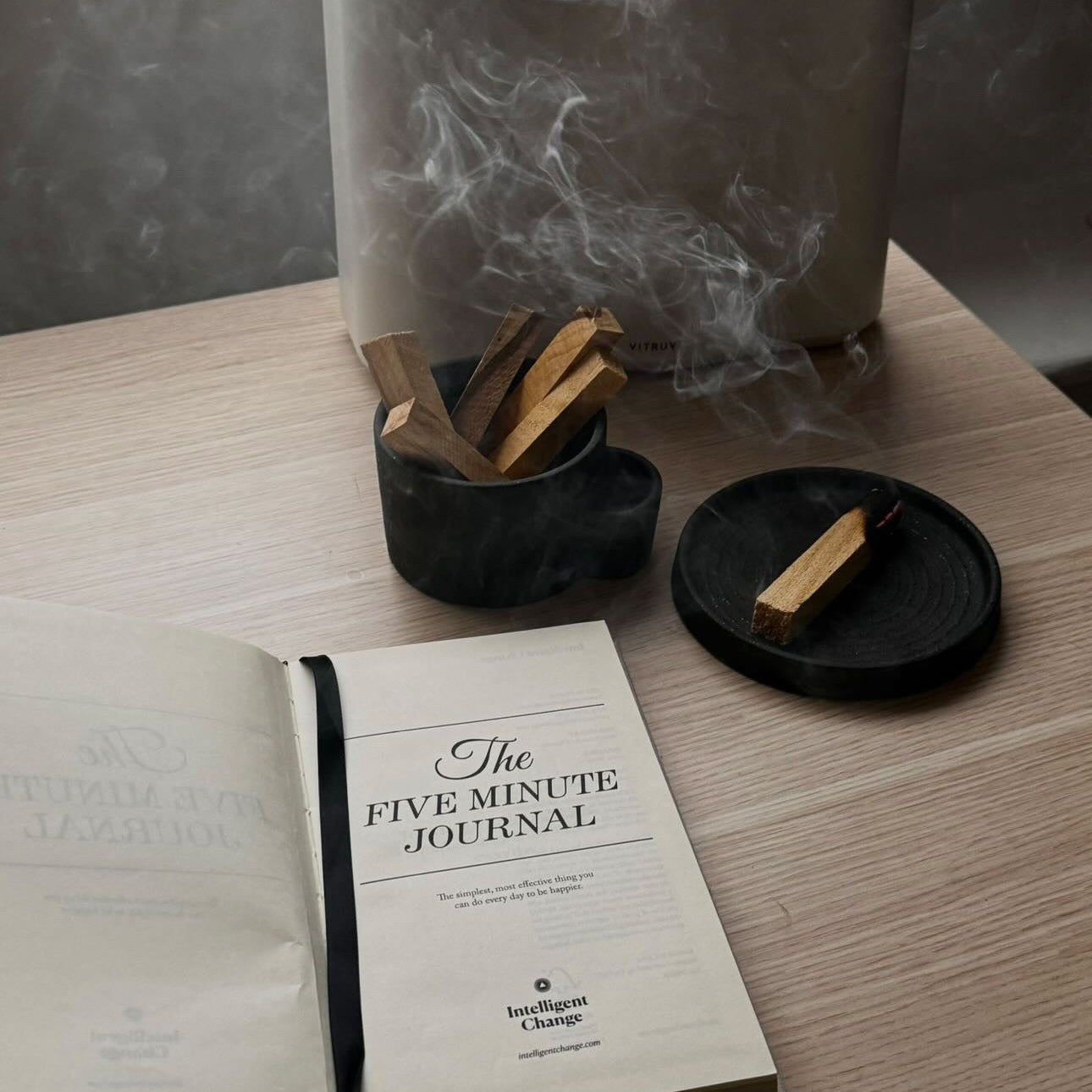 Book titled 'The Five Minute Journal' on a table with a diffuser and wooden sticks.