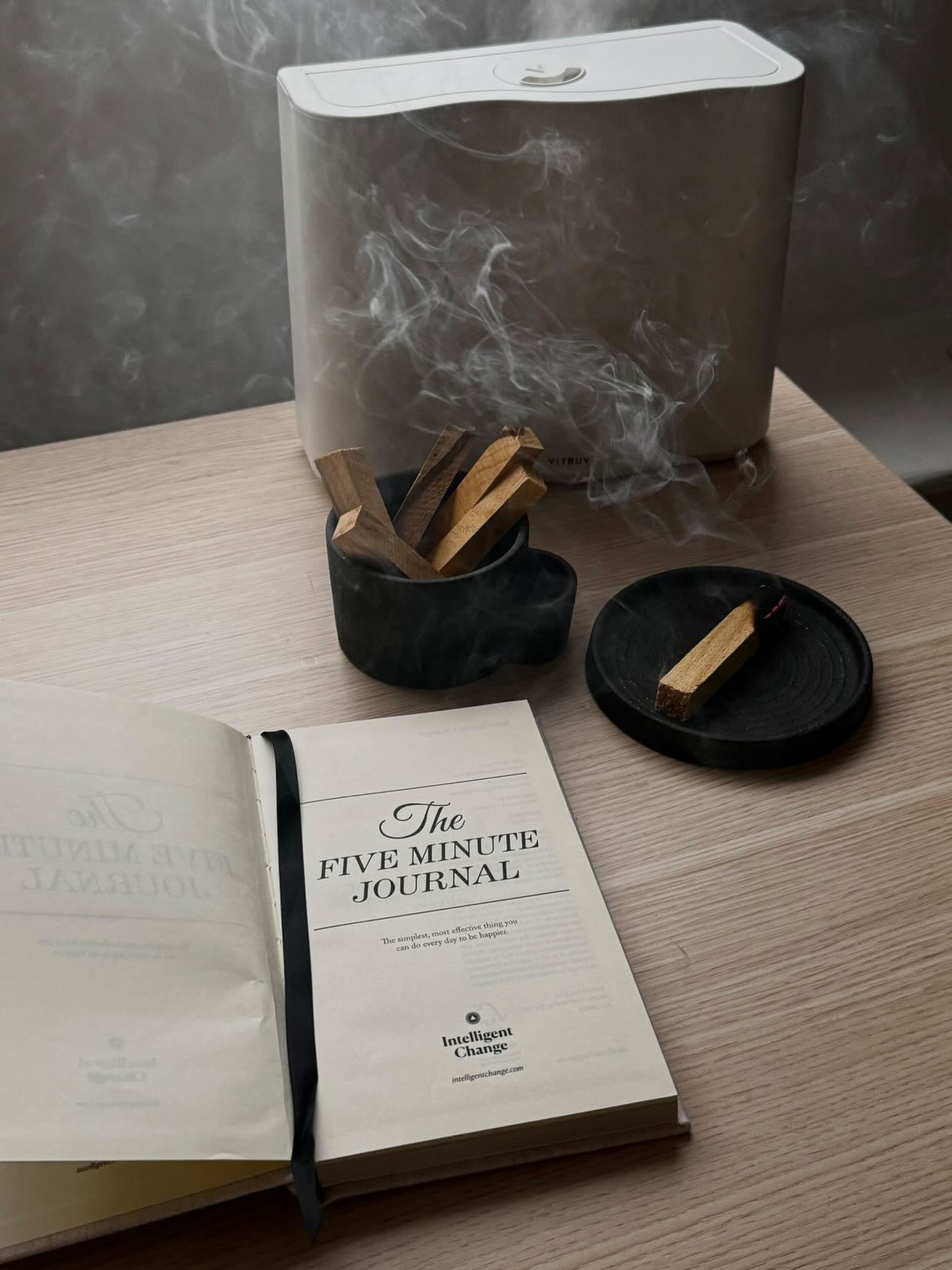 Book titled 'The Five Minute Journal' on a table with a diffuser and wooden sticks.