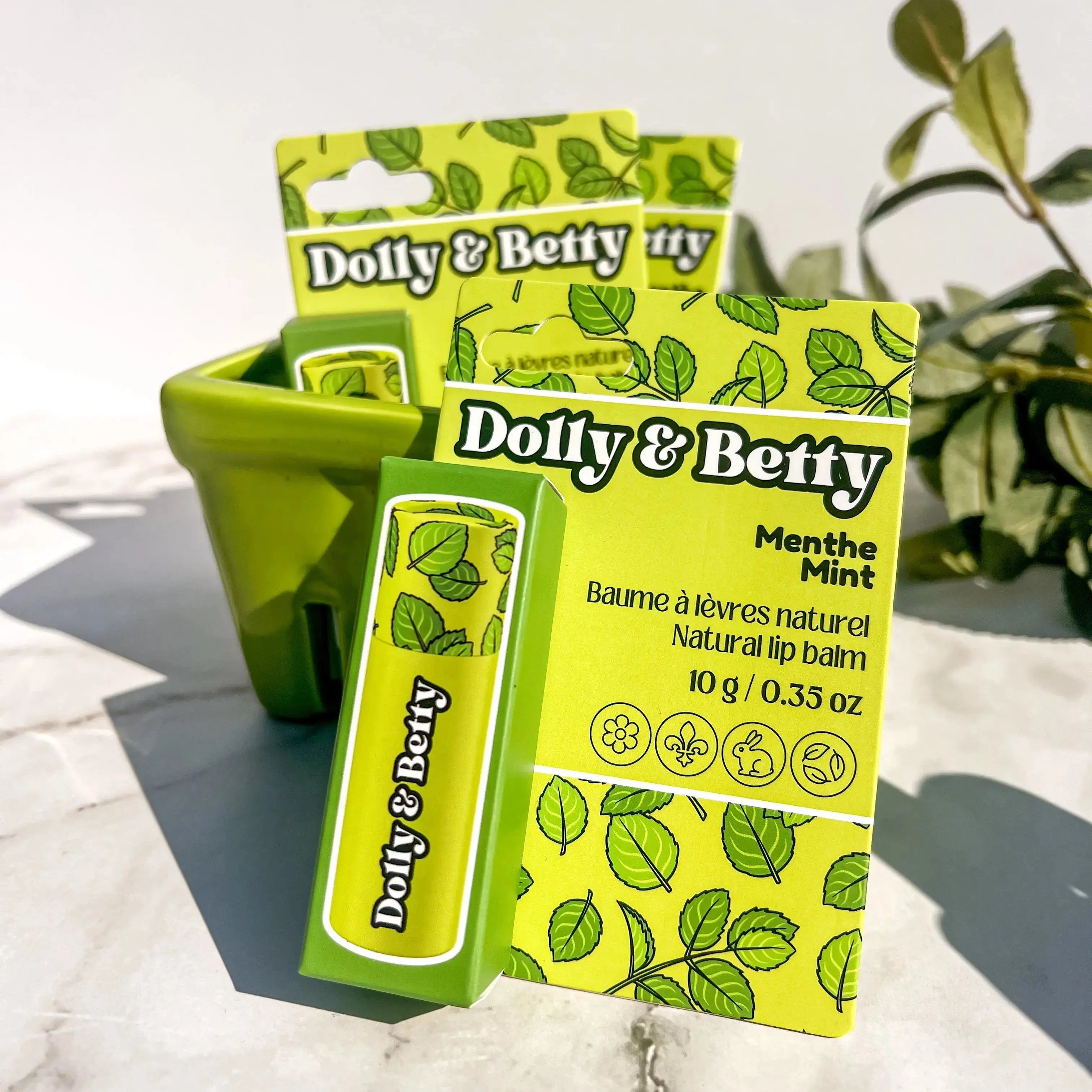 Dolly & Betty lip balm packaging with green plant in the background