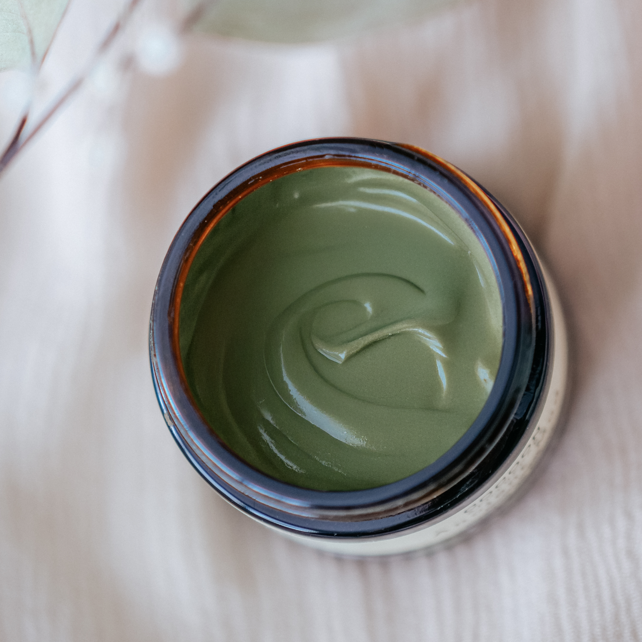 Jar of green cream with a visible brand logo on a light fabric background