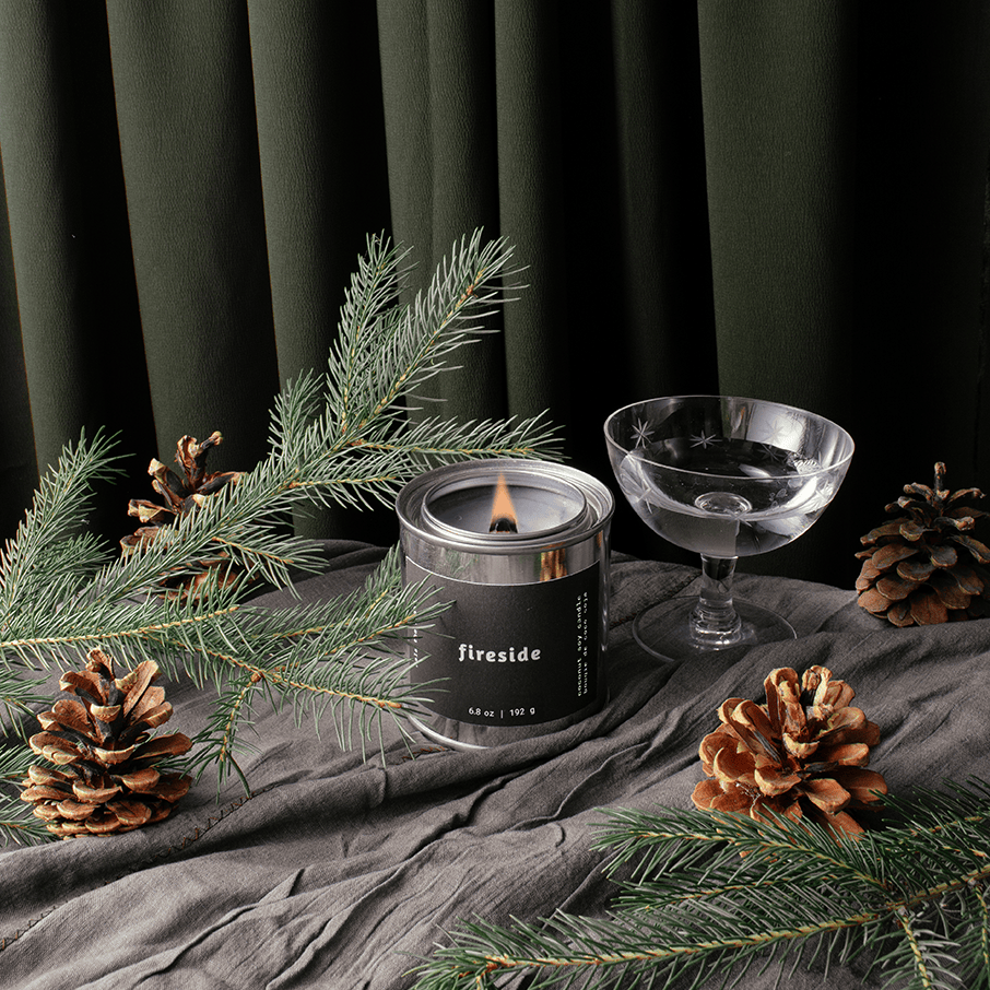 Candle labeled 'Fireside' with pine branches and pinecones on a dark background