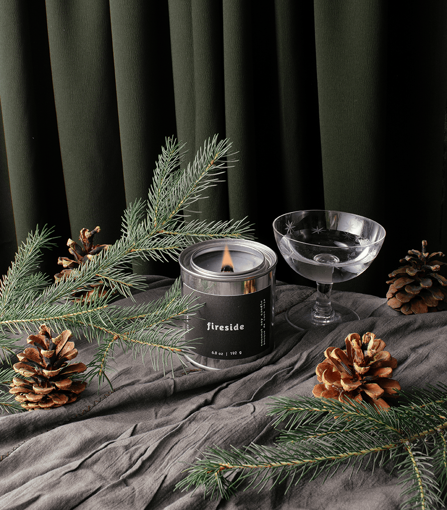 Candle labeled 'Fireside' with pine branches and pinecones on a dark background