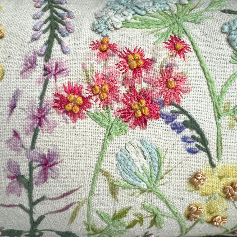 Embroidered floral design on fabric with pink flowers and green leaves.