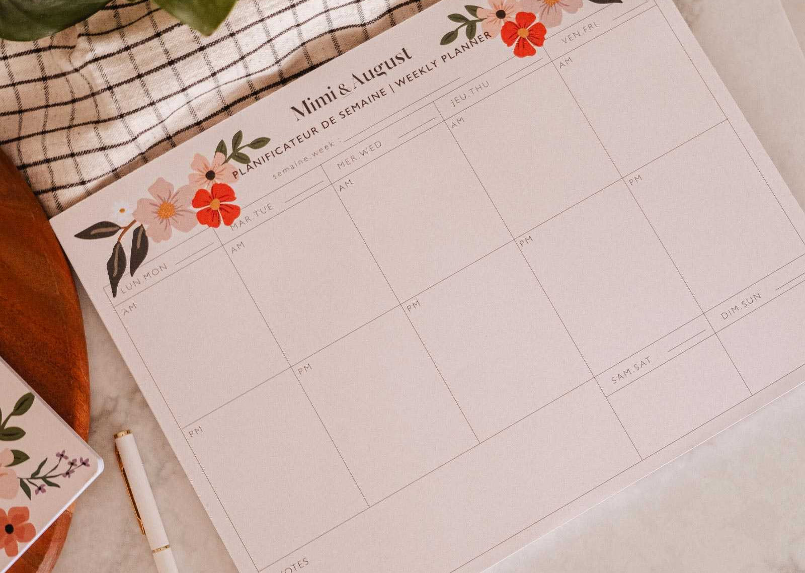 Floral-themed calendar on a marble surface with a pen and plant.