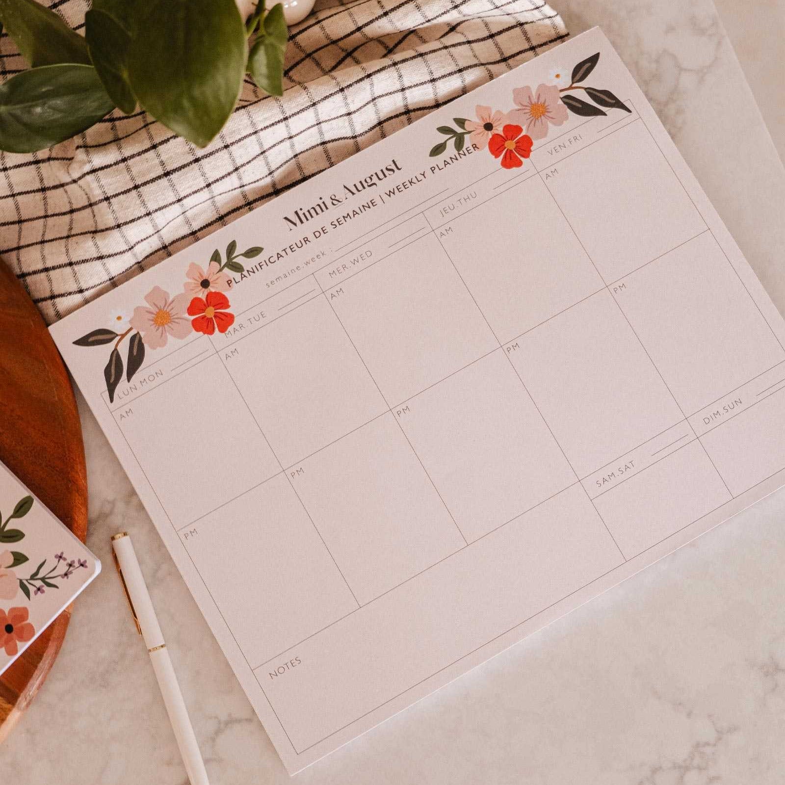 Floral-themed calendar on a marble surface with a pen and plant.