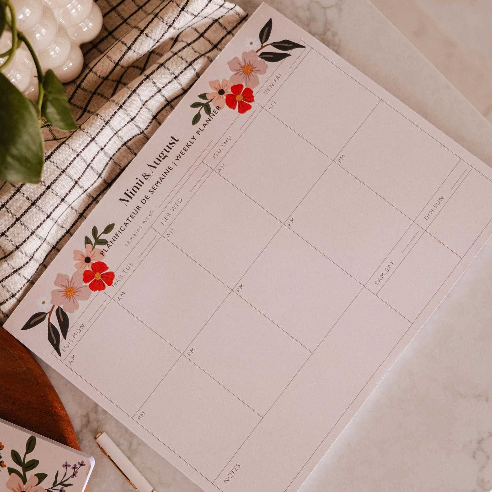 Floral planner sheet on a marble surface with a pen and plant.