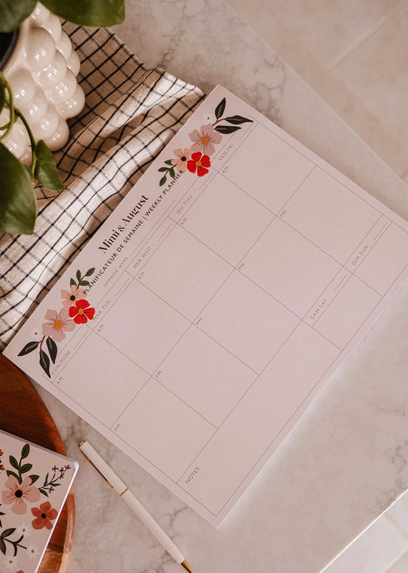 Floral planner sheet on a marble surface with a pen and plant.