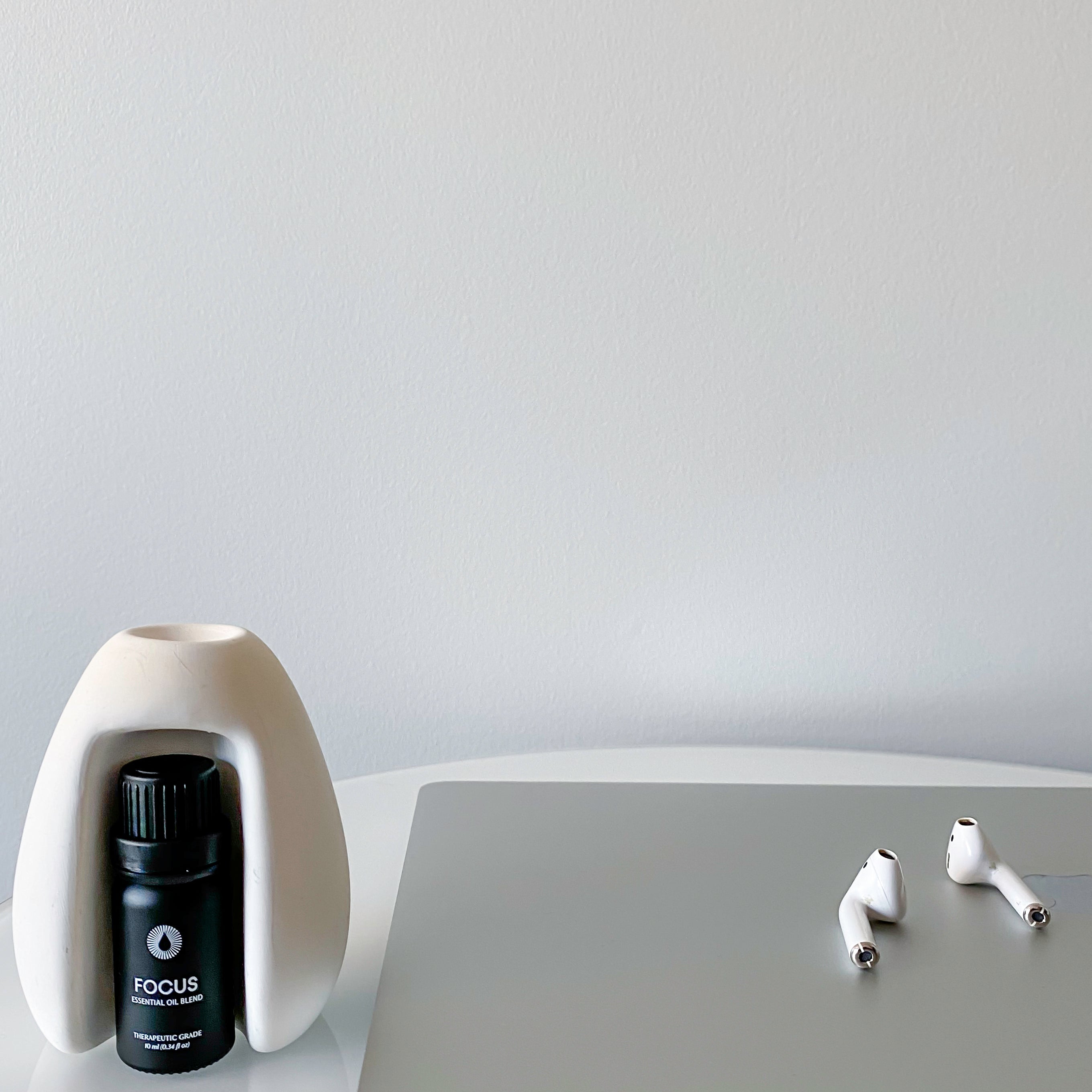 Laptop with earbuds and a bottle labeled 'FOCUS' on a white surface.