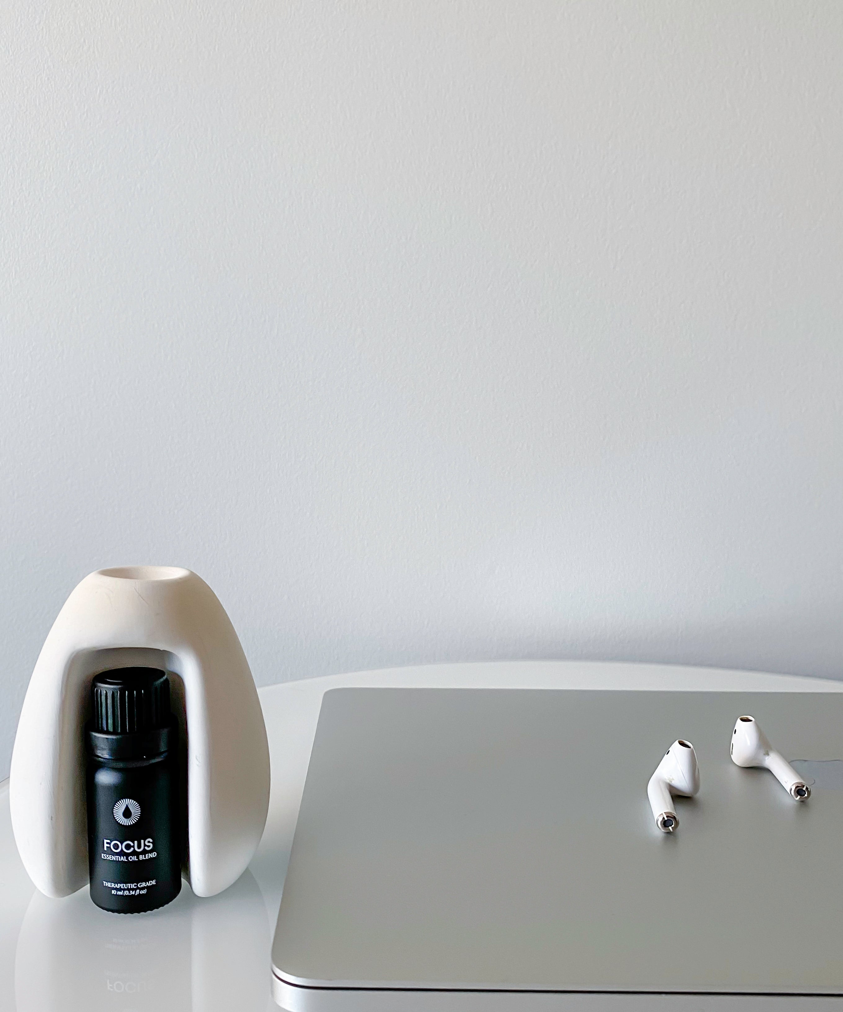Laptop with earbuds and a bottle labeled 'FOCUS' on a white surface.