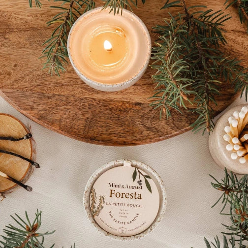 Candle on a wooden board with greenery and a branded candle lid. Foresta Reusable Candle by mimi and august