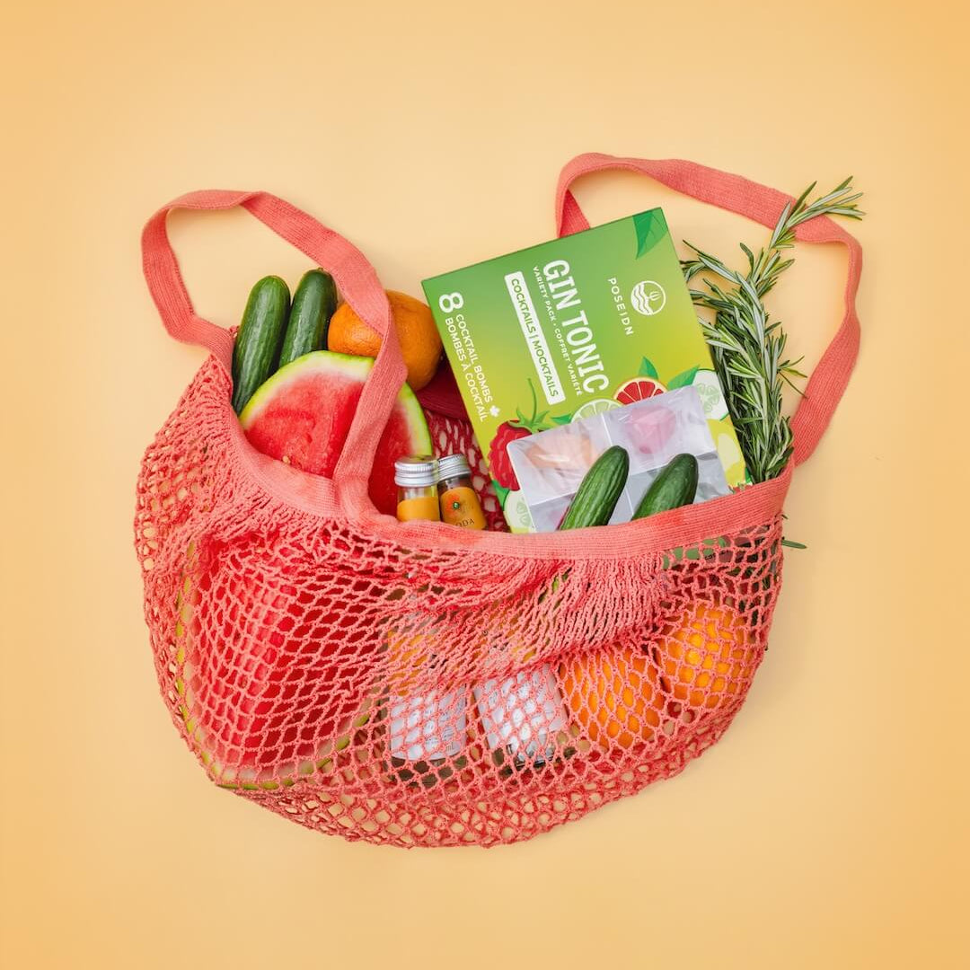 Red mesh bag filled with groceries including vegetables and a box on a yellow background