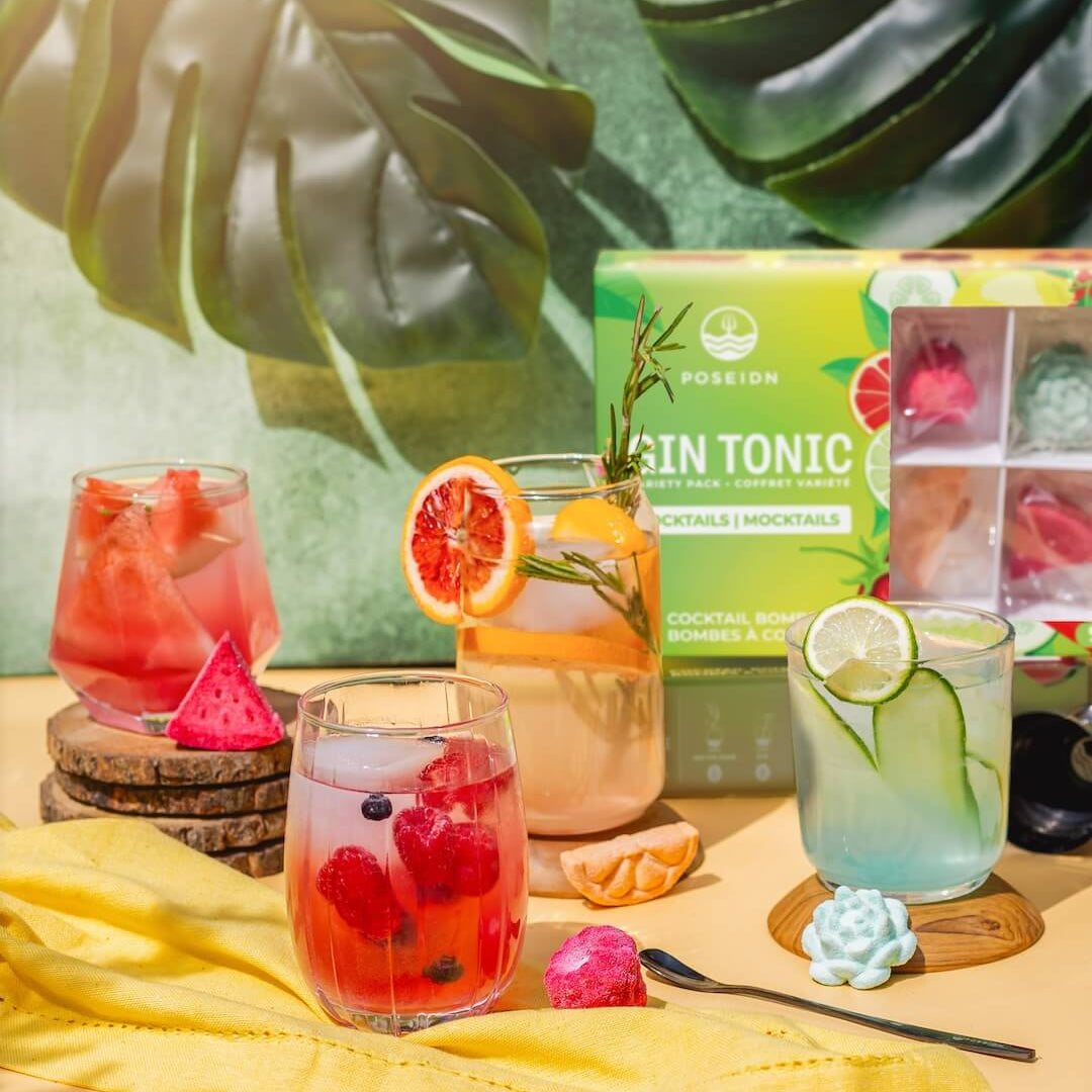 Assorted cocktails with garnishes and a box of tonics on a yellow cloth with green leafy background