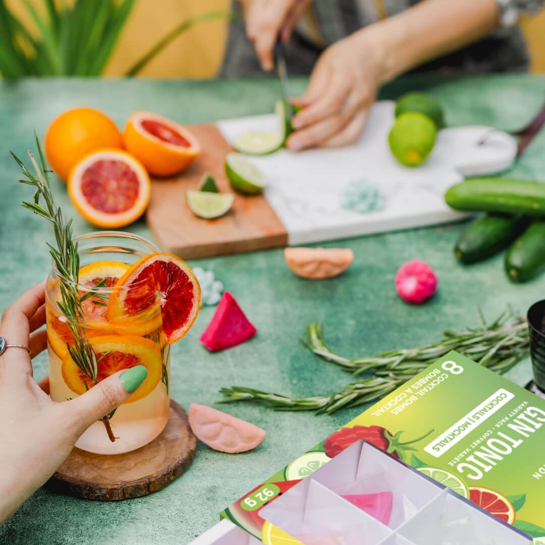 Person holding a glass of fruit-infused water on a table with ingredients and a box of tea bags.