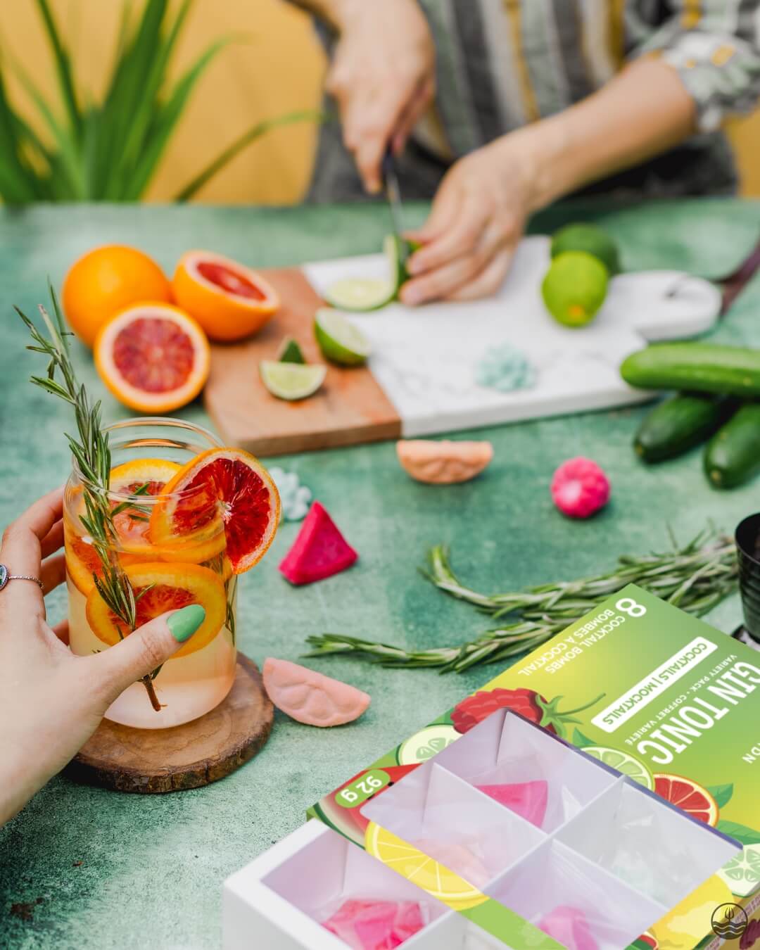 Person holding a glass of fruit-infused water on a table with ingredients and a box of tea bags.