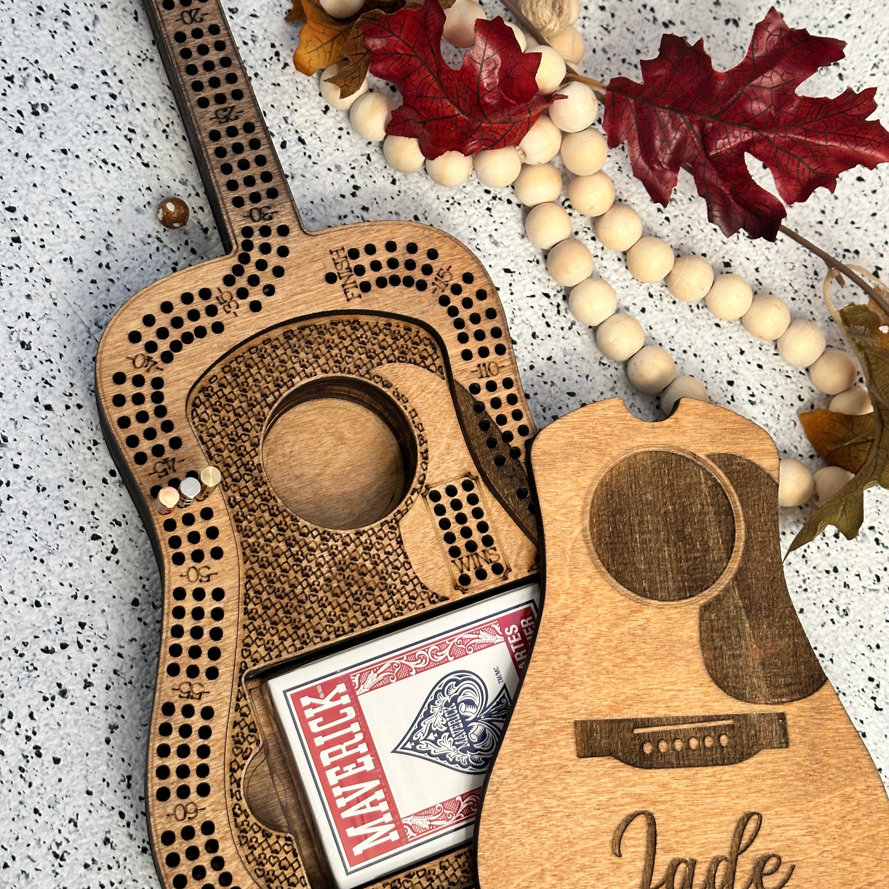 Wooden guitar-shaped cribbage board with card holder and beads on a textured surface.