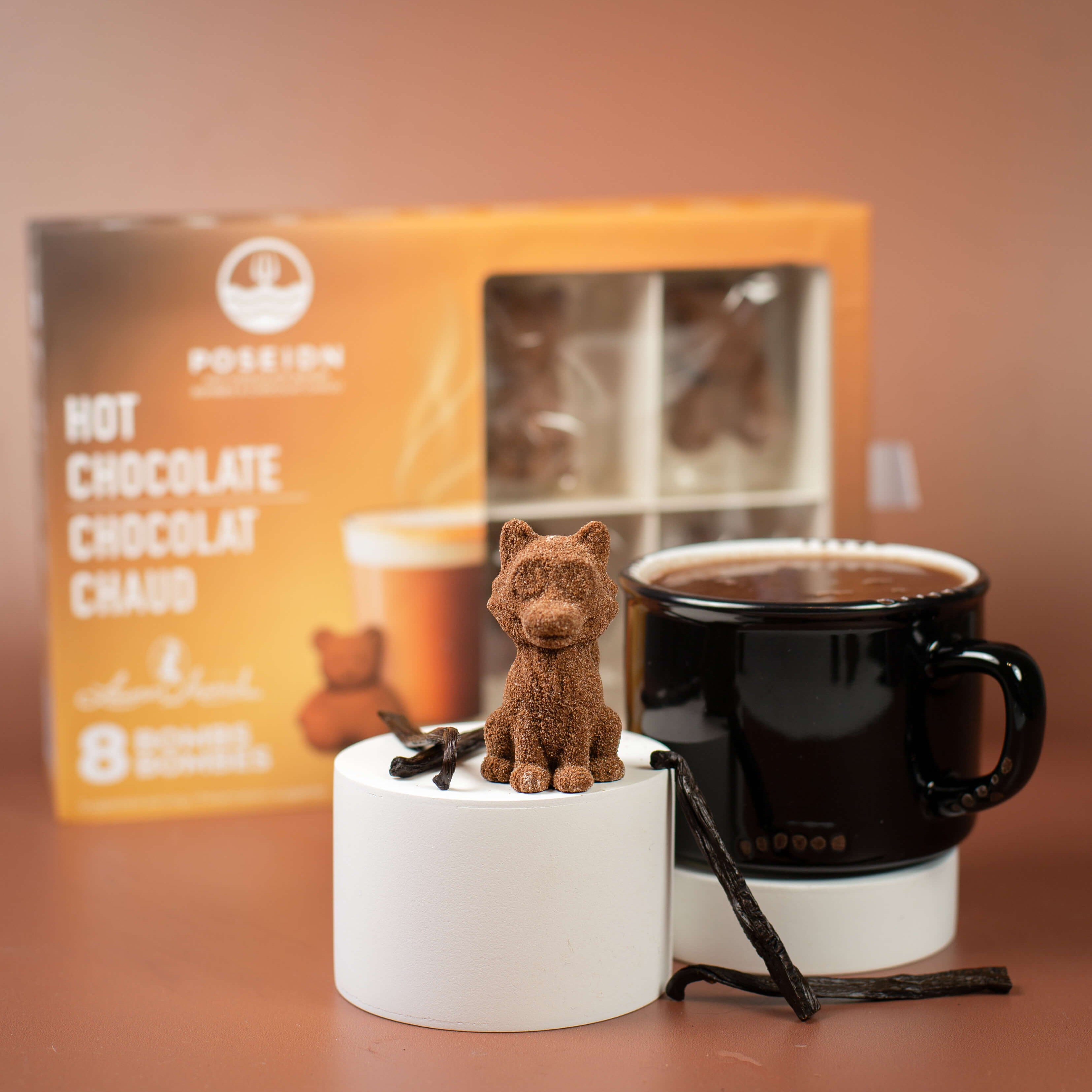 Hot chocolate with a small bear figurine and vanilla beans, featuring a Poscaion product in the background.
