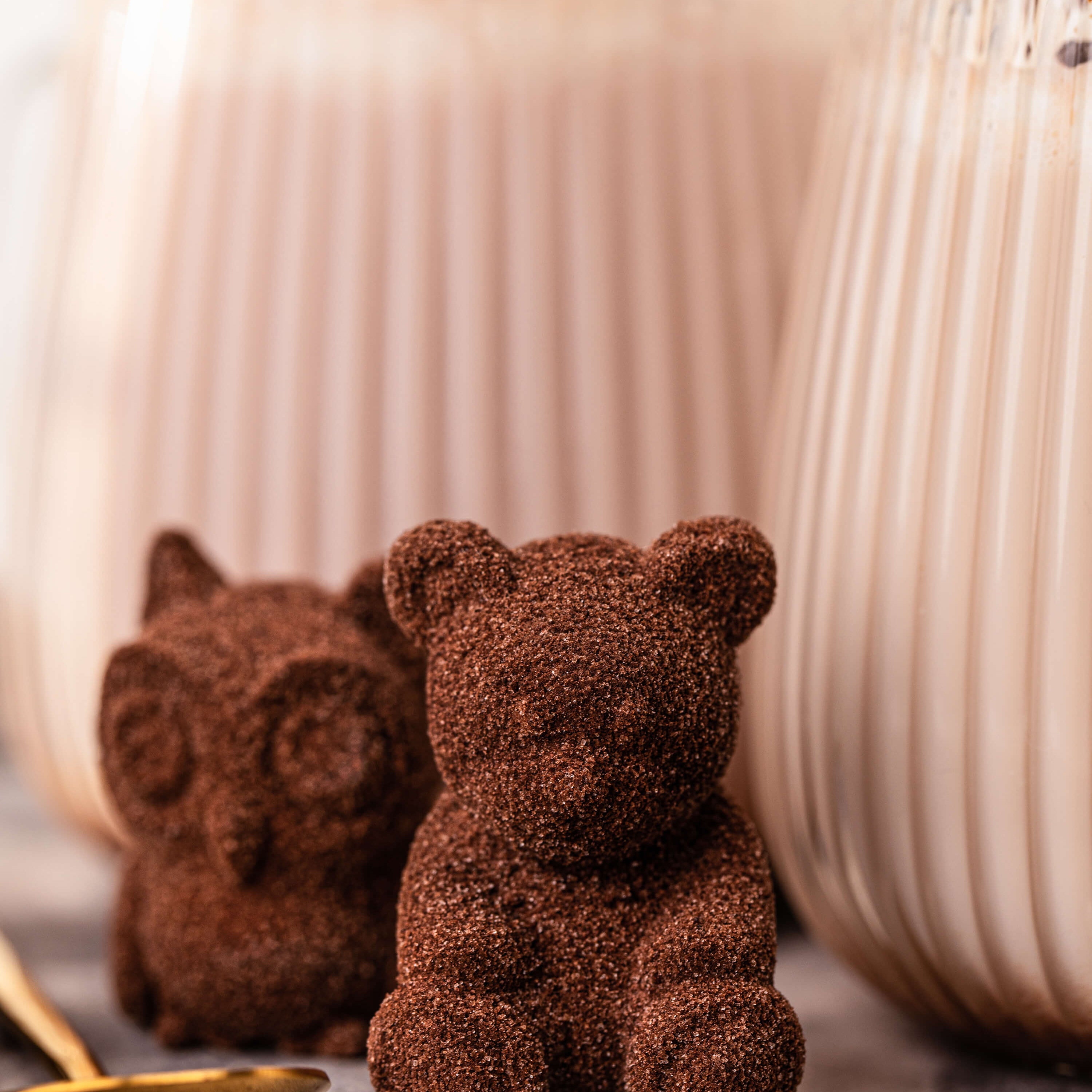 Two chocolate bear figurines in front of two glasses on a marble surface.