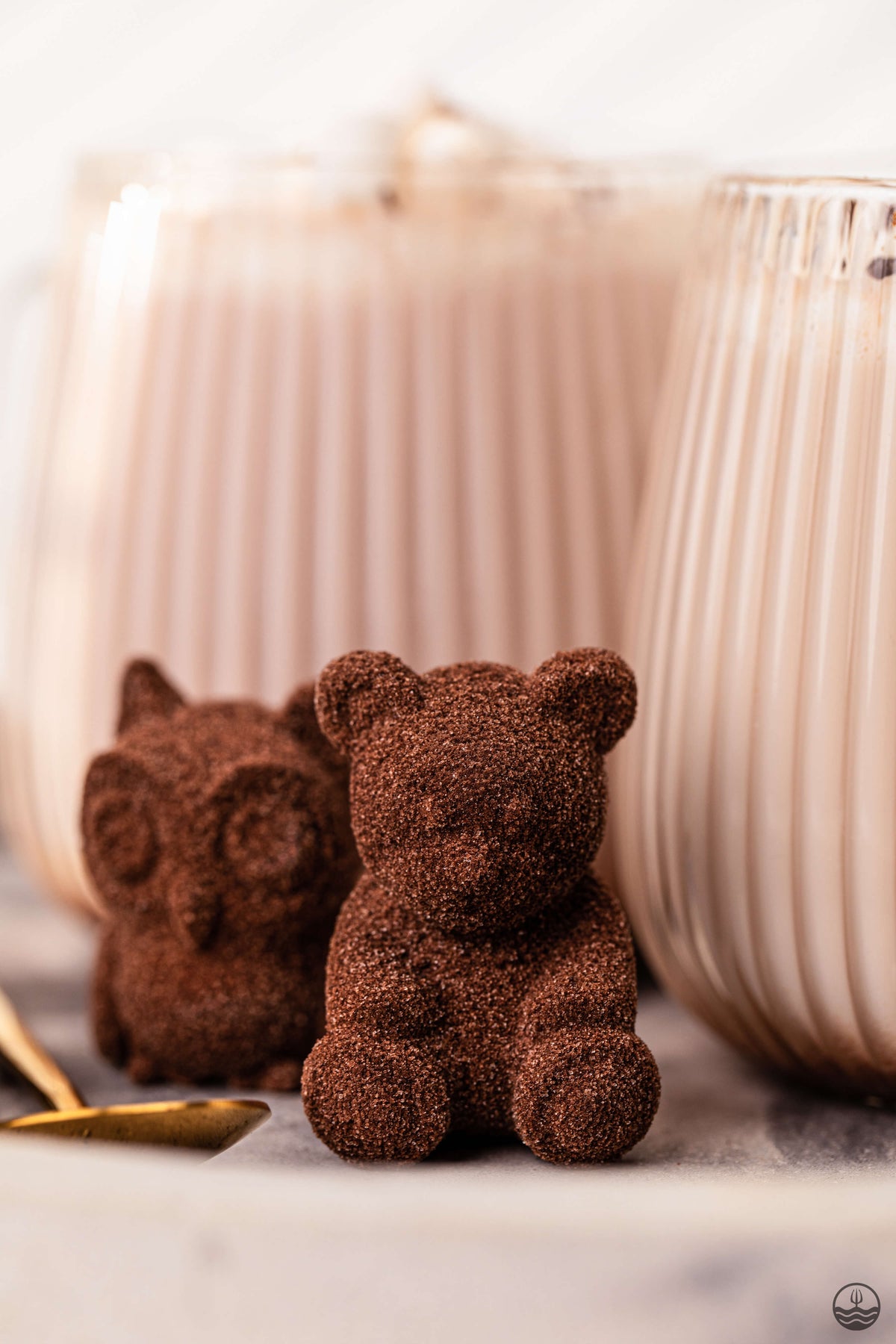 Two chocolate bear figurines in front of two glasses on a marble surface.