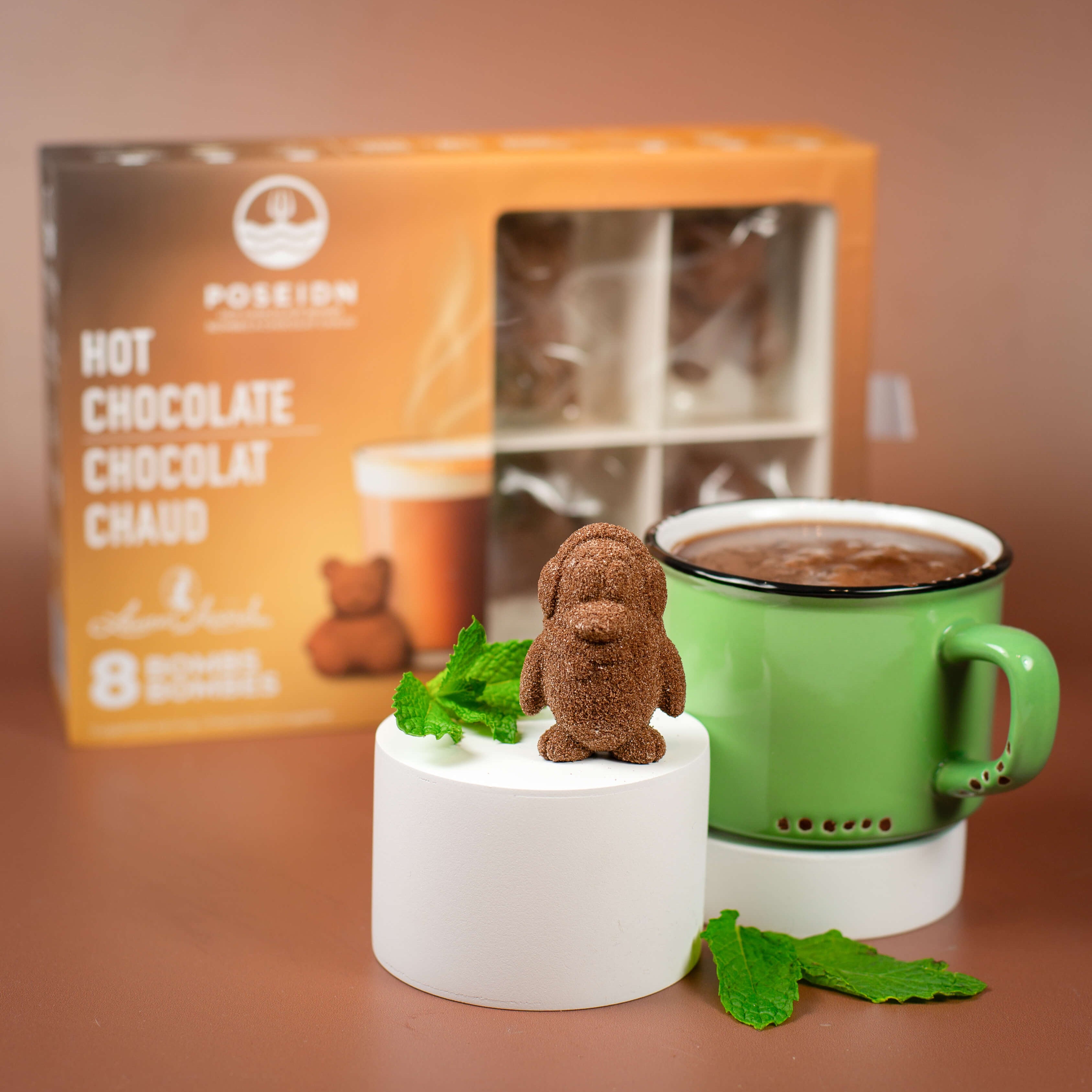 Hot chocolate mug with a bear-shaped chocolate cube and mint leaves, next to a Posseion Hot Chocolate box.