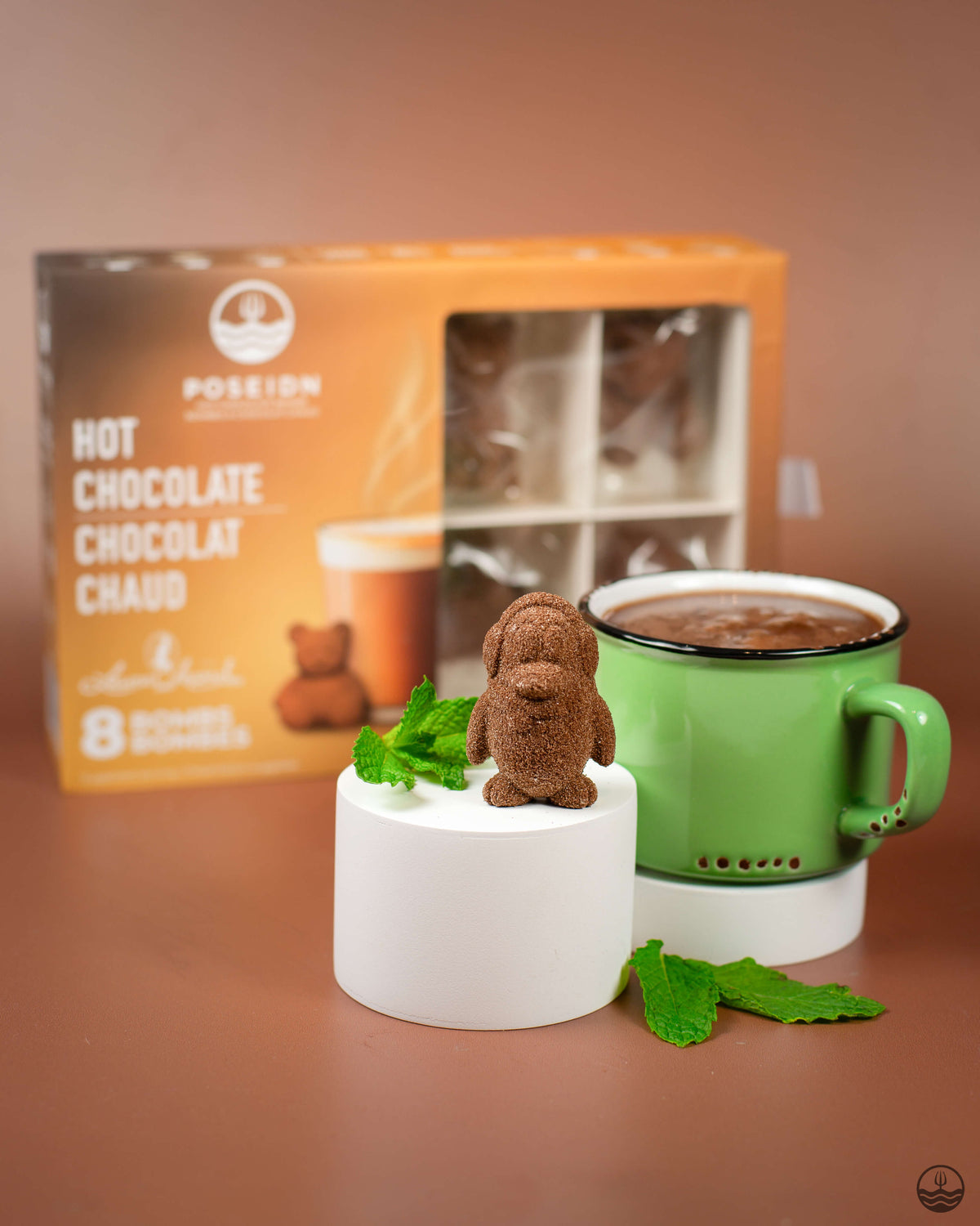 Hot chocolate mug with a bear-shaped chocolate cube and mint leaves, next to a Posseion Hot Chocolate box.