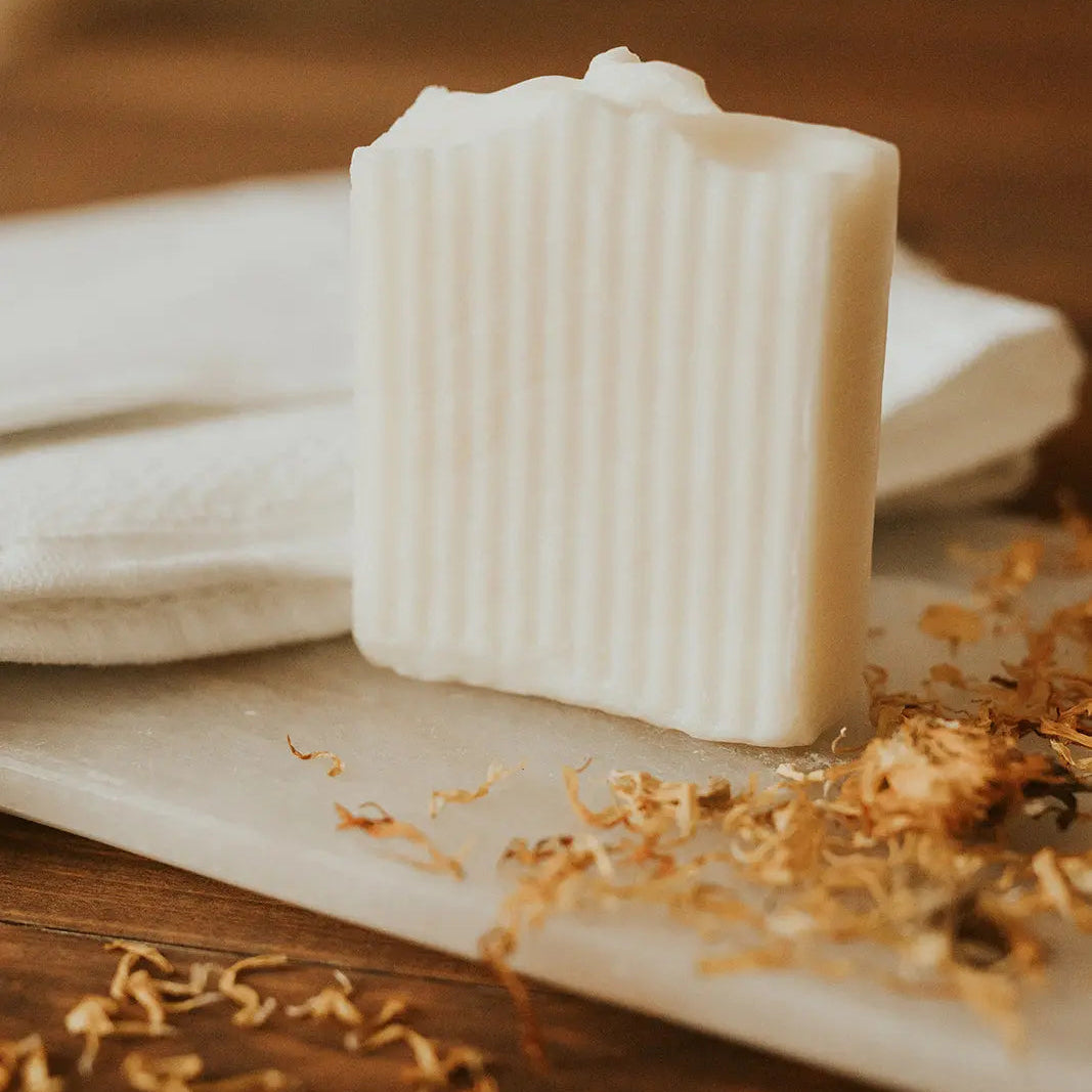 Bar of soap on a wooden surface with dried flowers and a white cloth.
