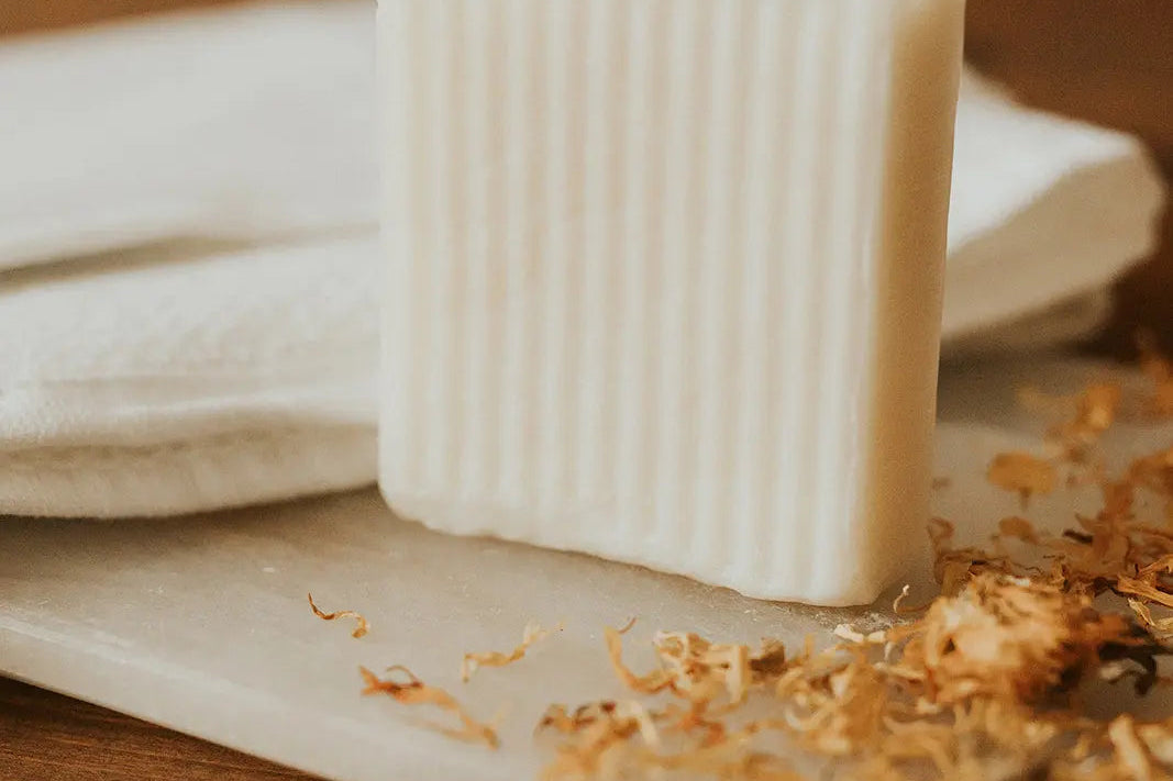 Bar of soap on a wooden surface with dried flowers and a white cloth.
