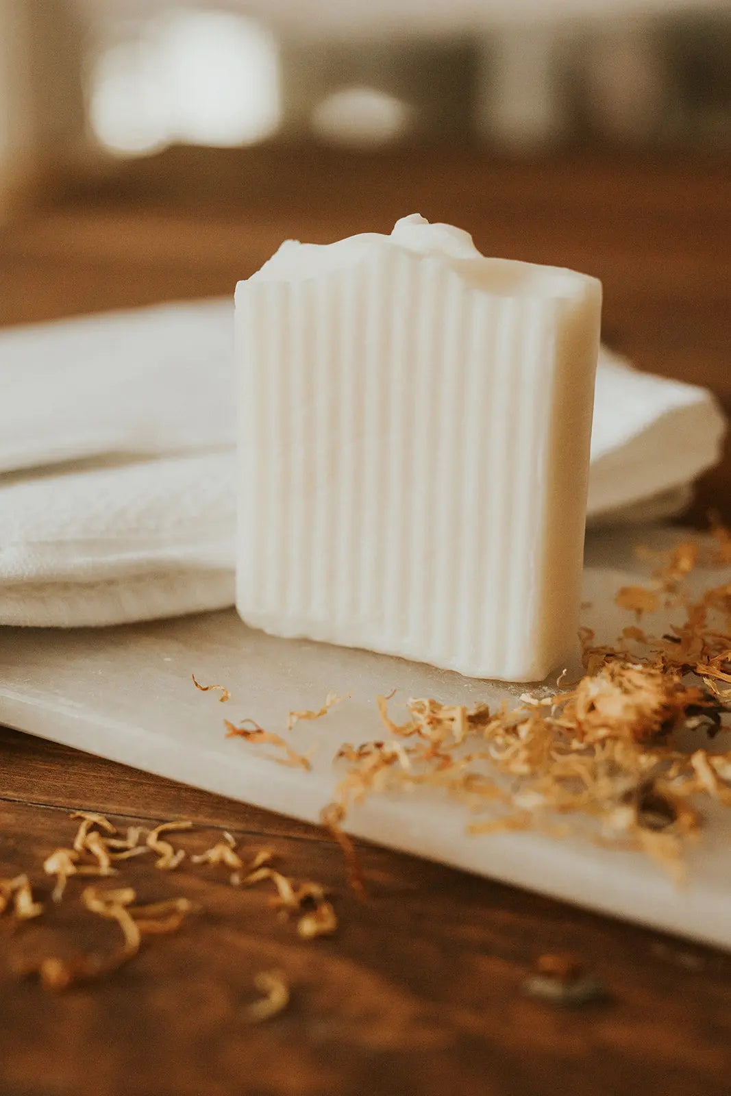 Bar of soap on a wooden surface with dried flowers and a white cloth.