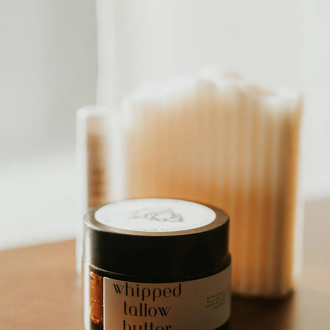 Jar of whipped follow butter on a wooden surface with a blurred candle in the background