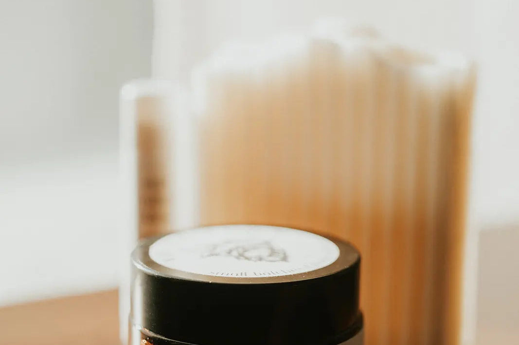 Jar of whipped follow butter on a wooden surface with a blurred candle in the background
