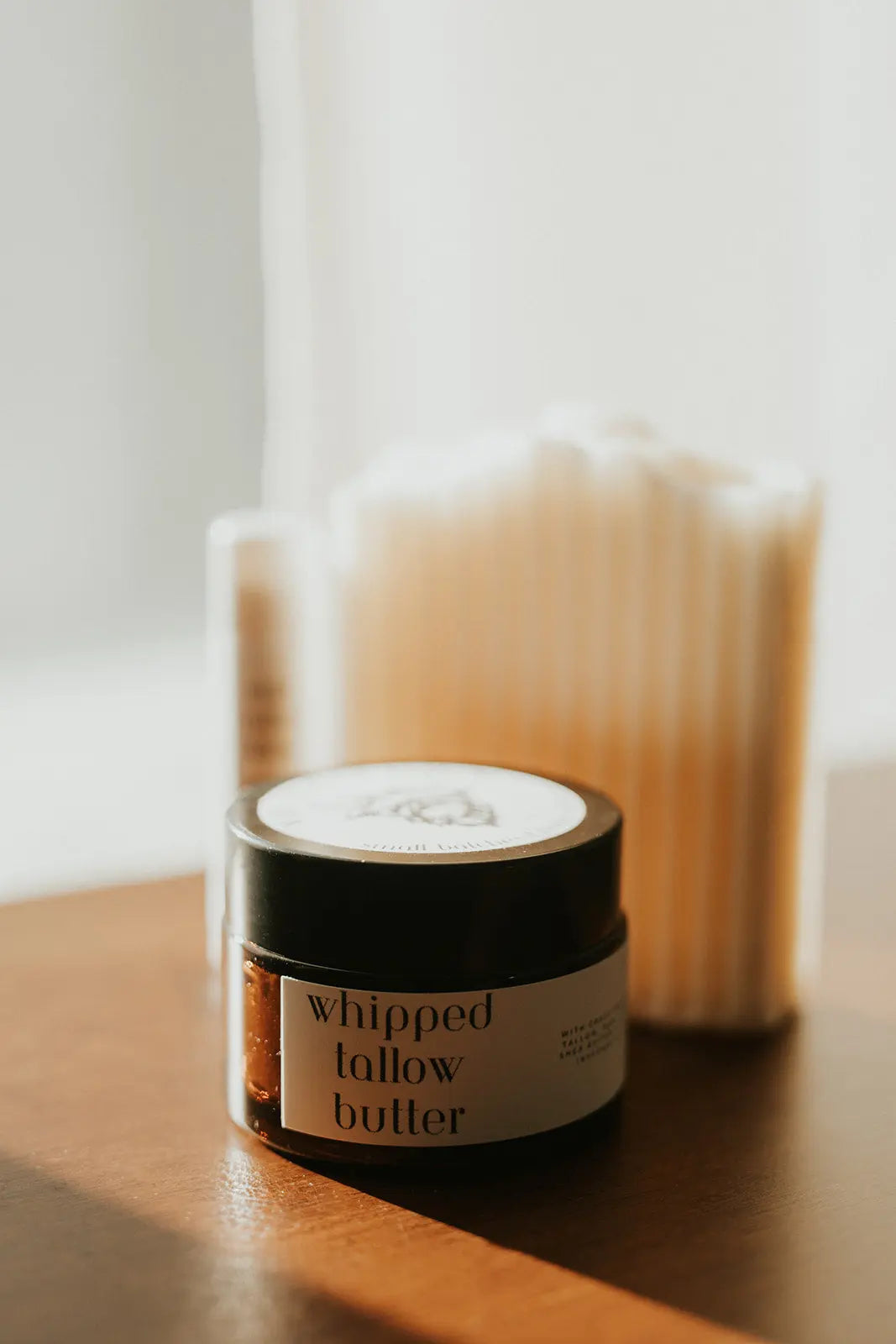 Jar of whipped follow butter on a wooden surface with a blurred candle in the background