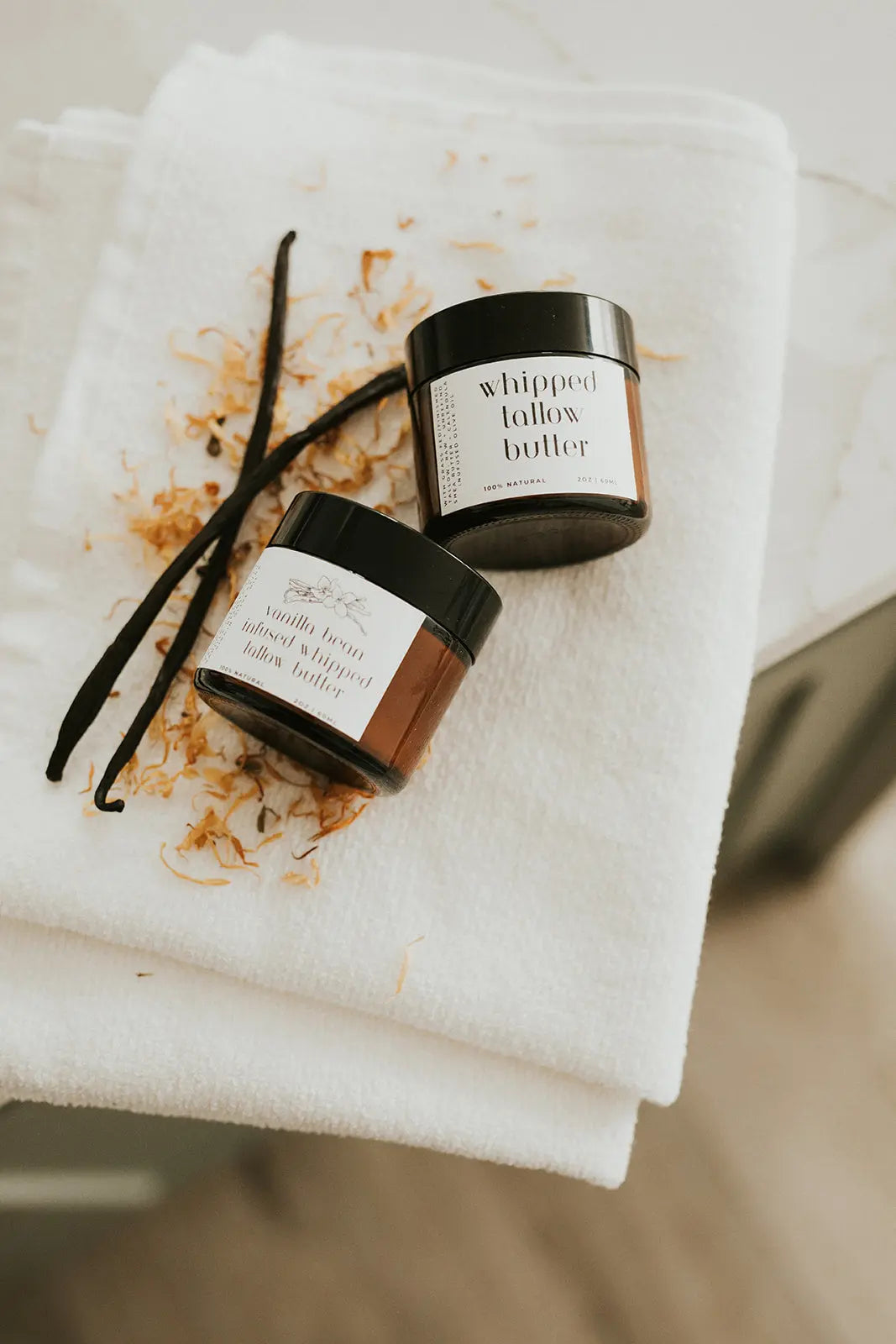 Two containers of whipped butter on a white towel with a vanilla bean.