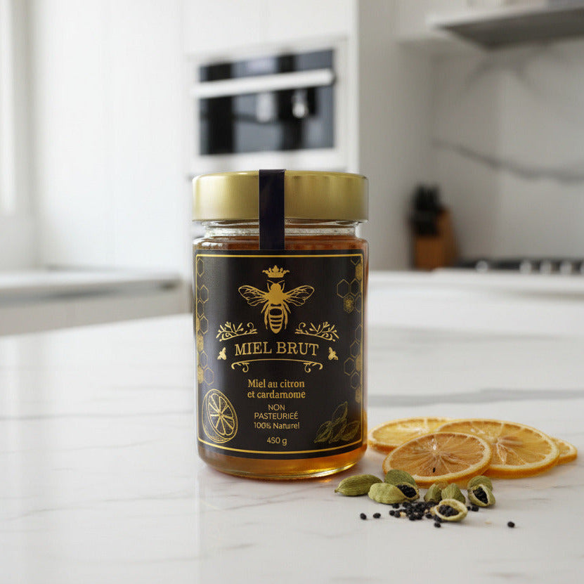 Jar of Miel Brut honey on a kitchen counter with dried oranges and cardamom pods.