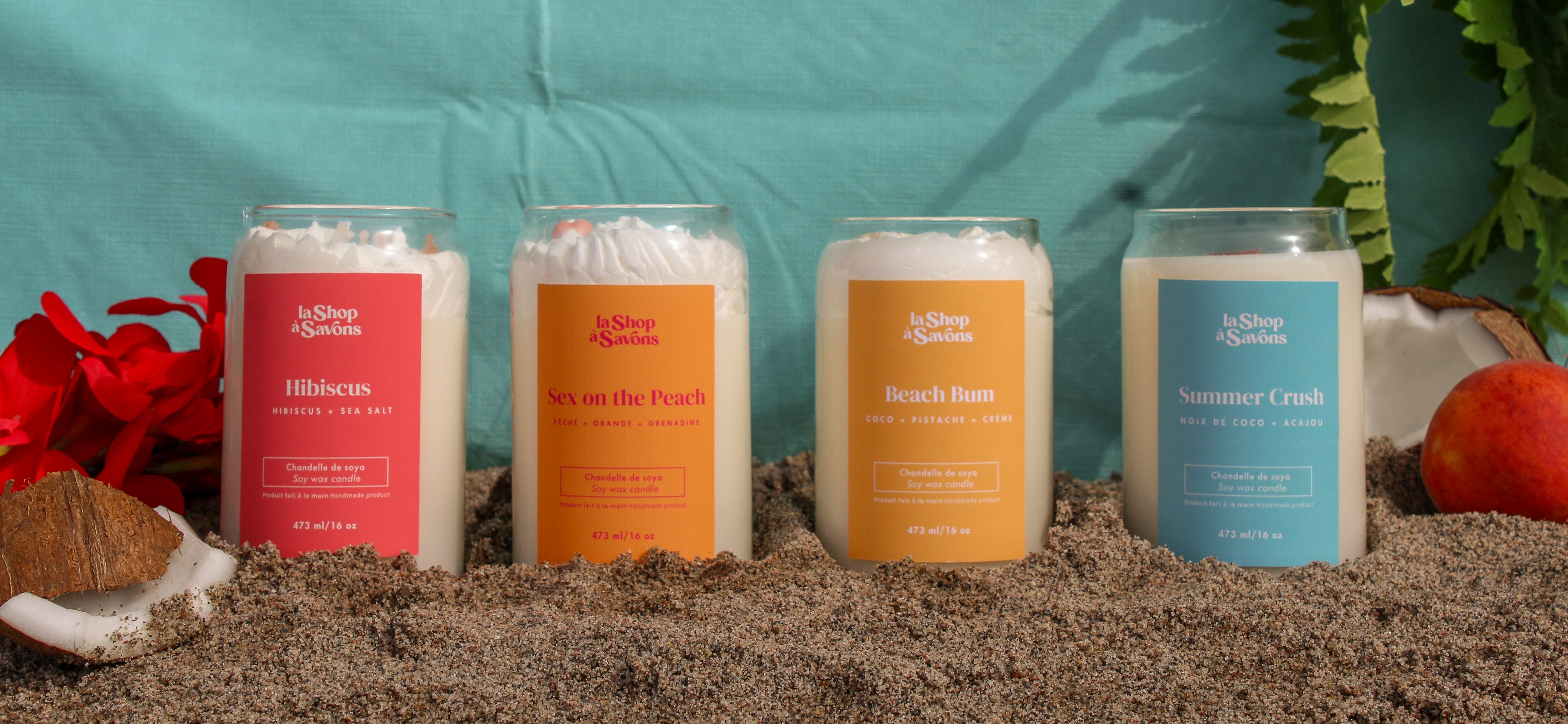 Four candles of different colors arranged on a sandy surface with a blue background