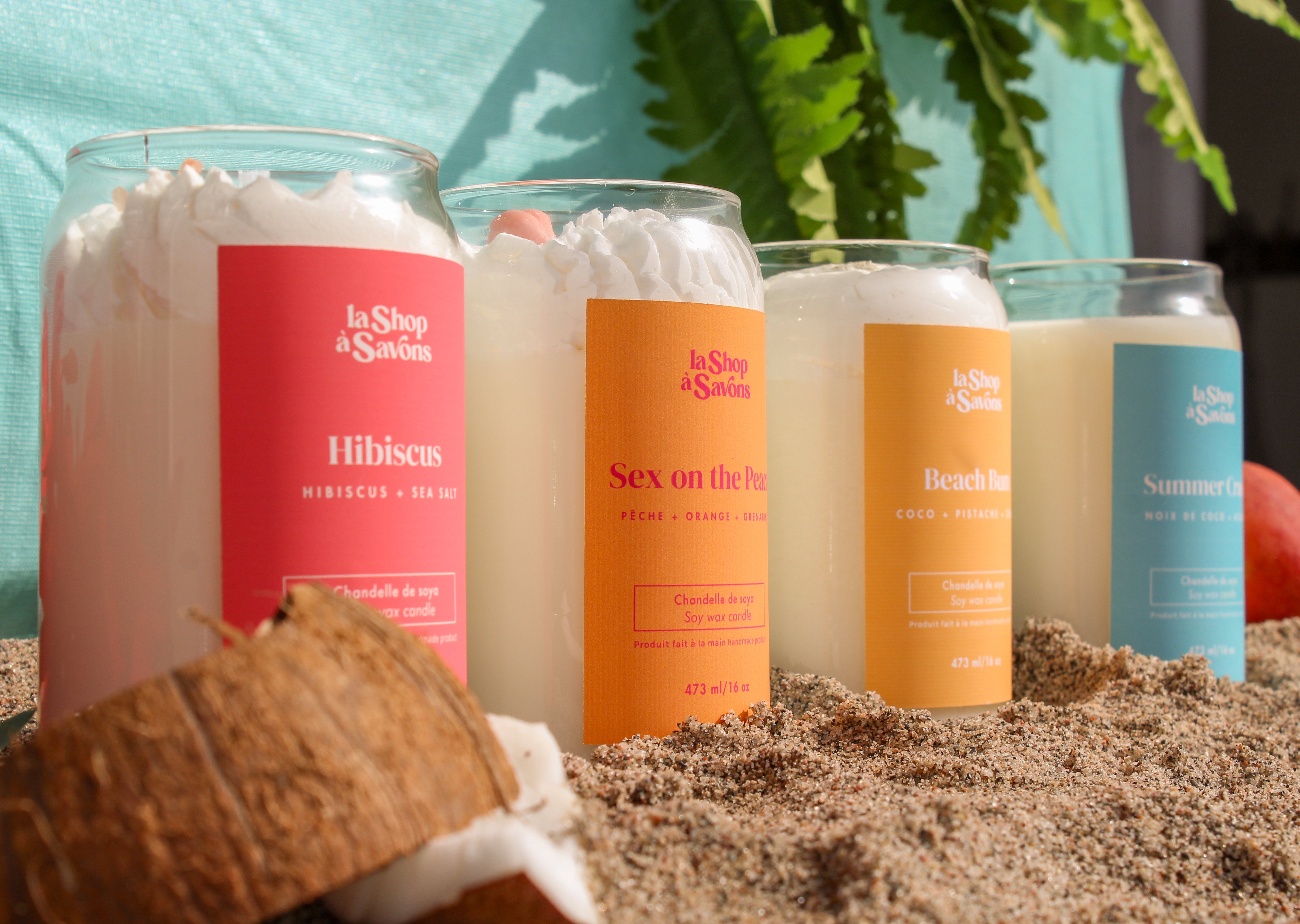 Set of candles with colorful labels on a sandy surface with plants in the background