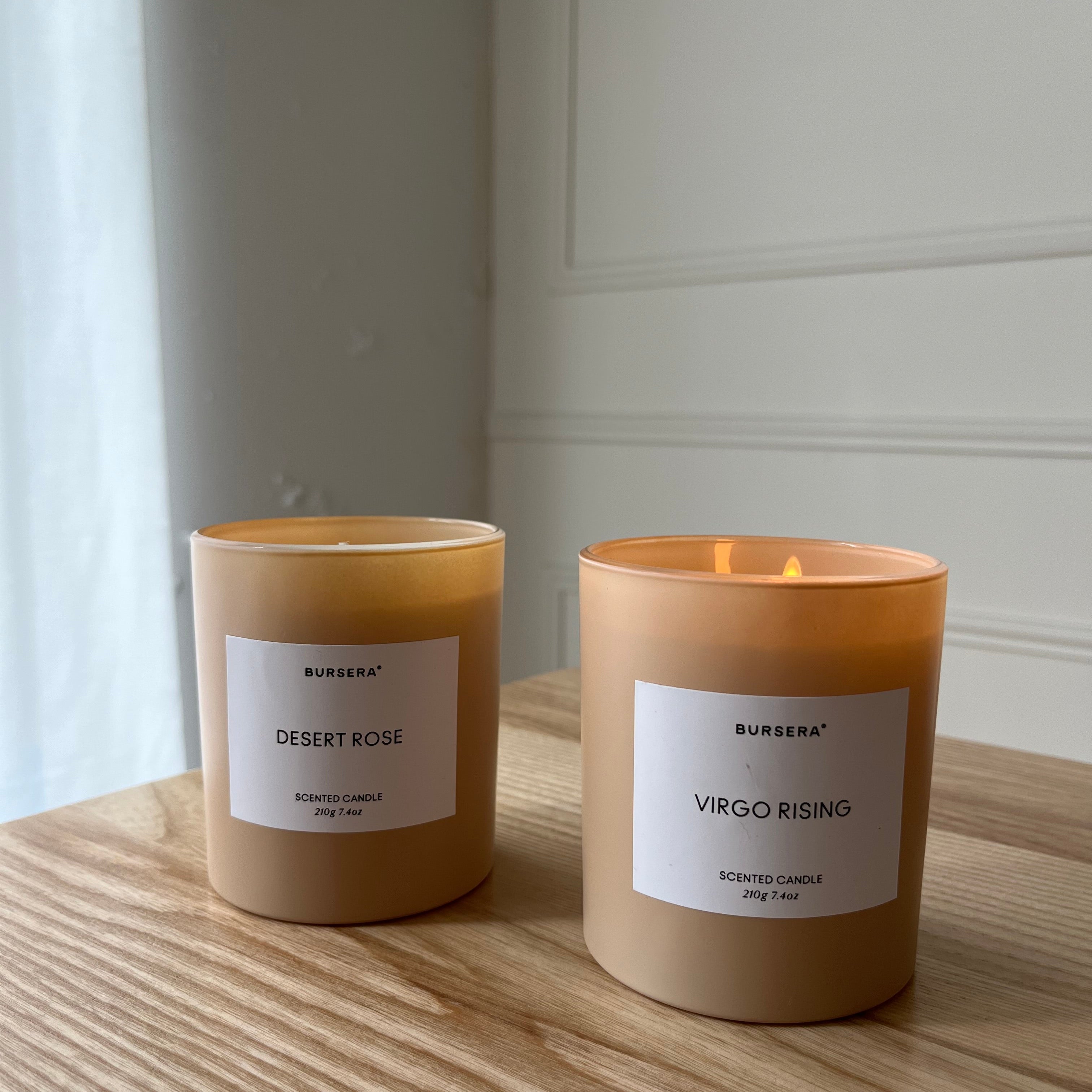 Two candles labeled 'Desert Rose' and 'Virgo Rising' on a wooden surface with a neutral background.