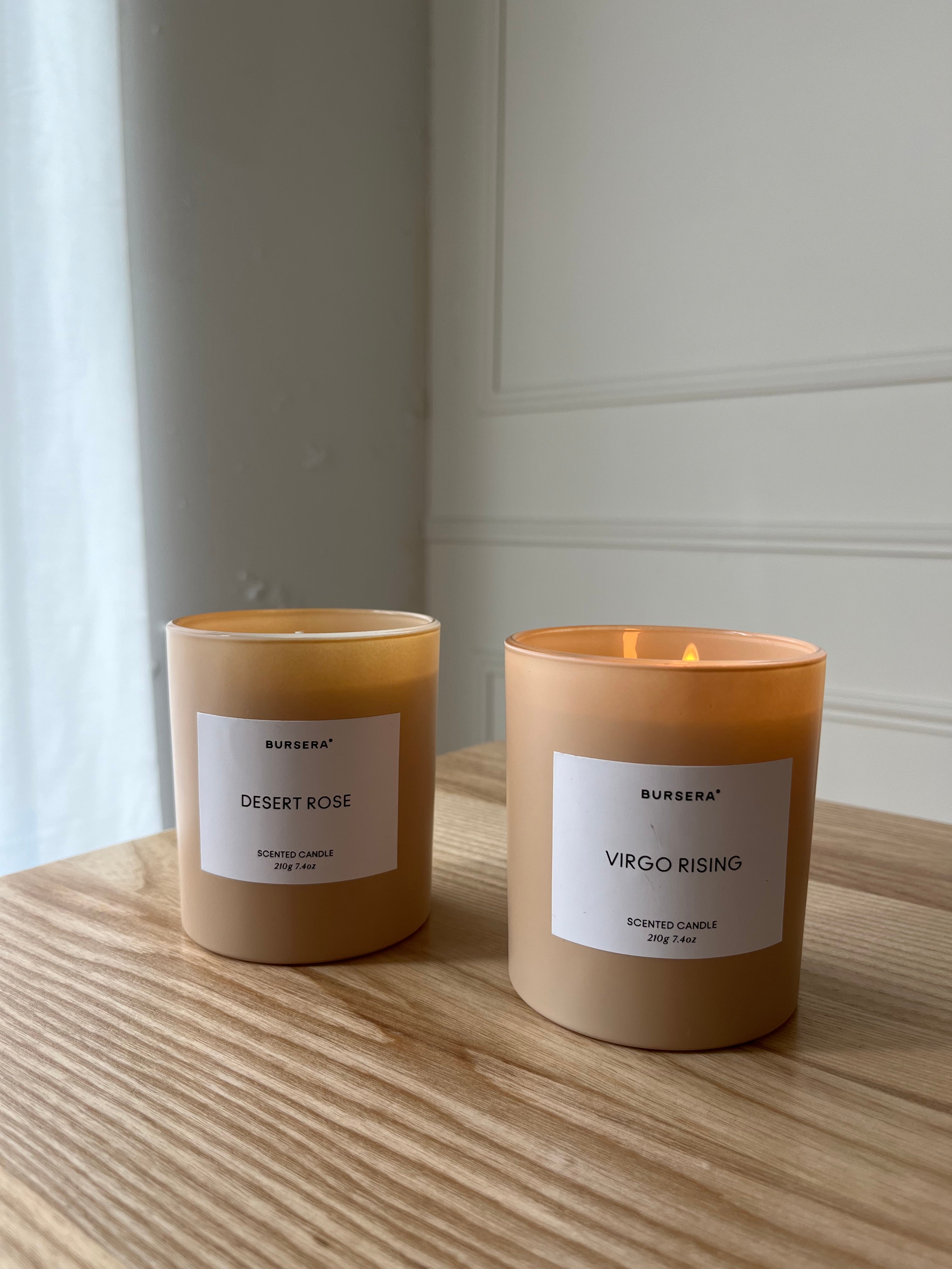 Two candles labeled 'Desert Rose' and 'Virgo Rising' on a wooden surface with a neutral background.