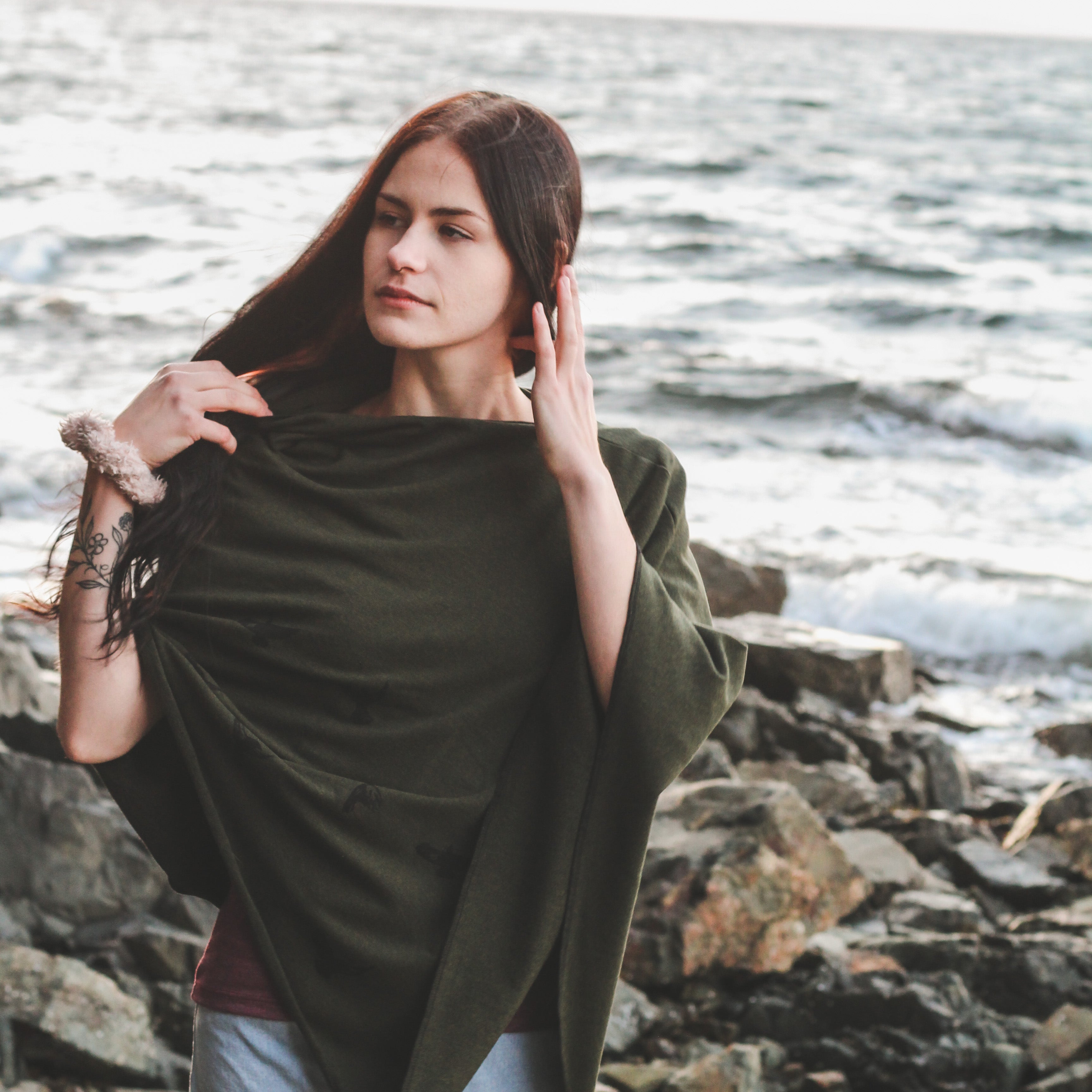 Woman standing on a rocky shoreline wearing a green shawl.