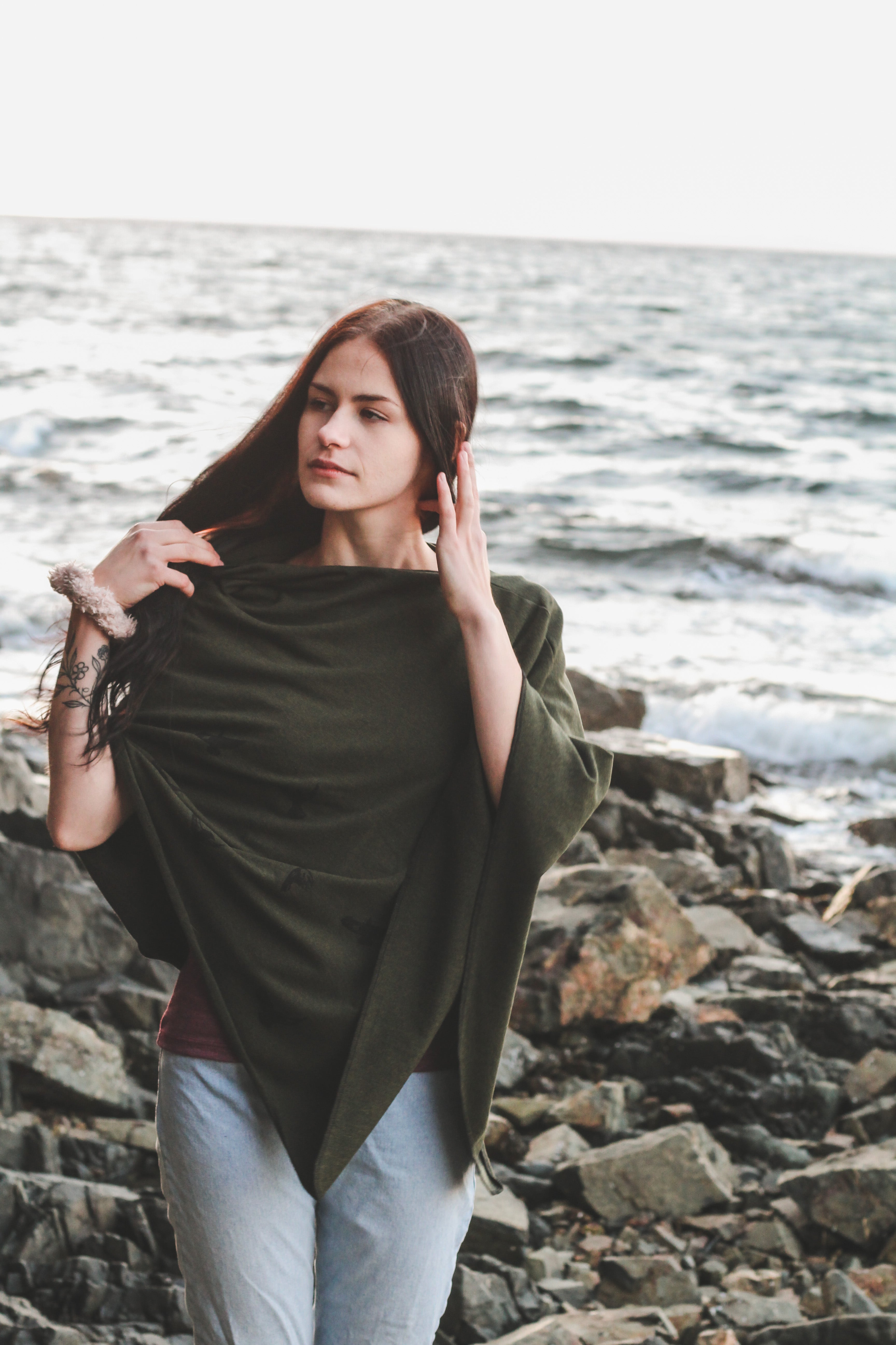 Woman standing on a rocky shoreline wearing a green shawl.