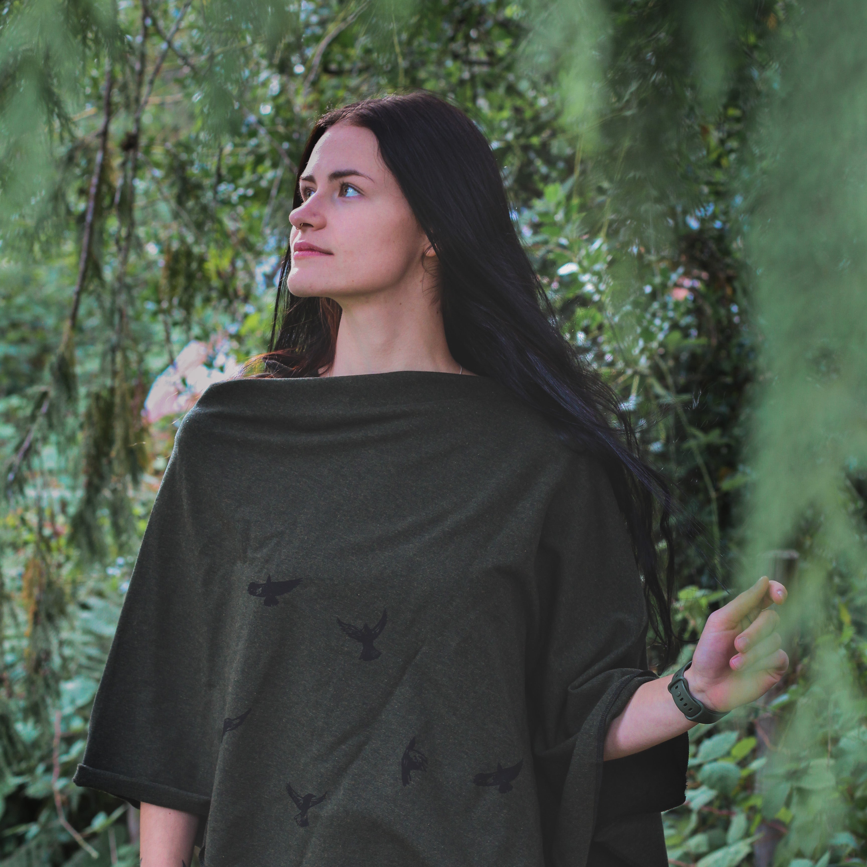 Woman wearing a dark green poncho with butterfly patterns in a forest setting