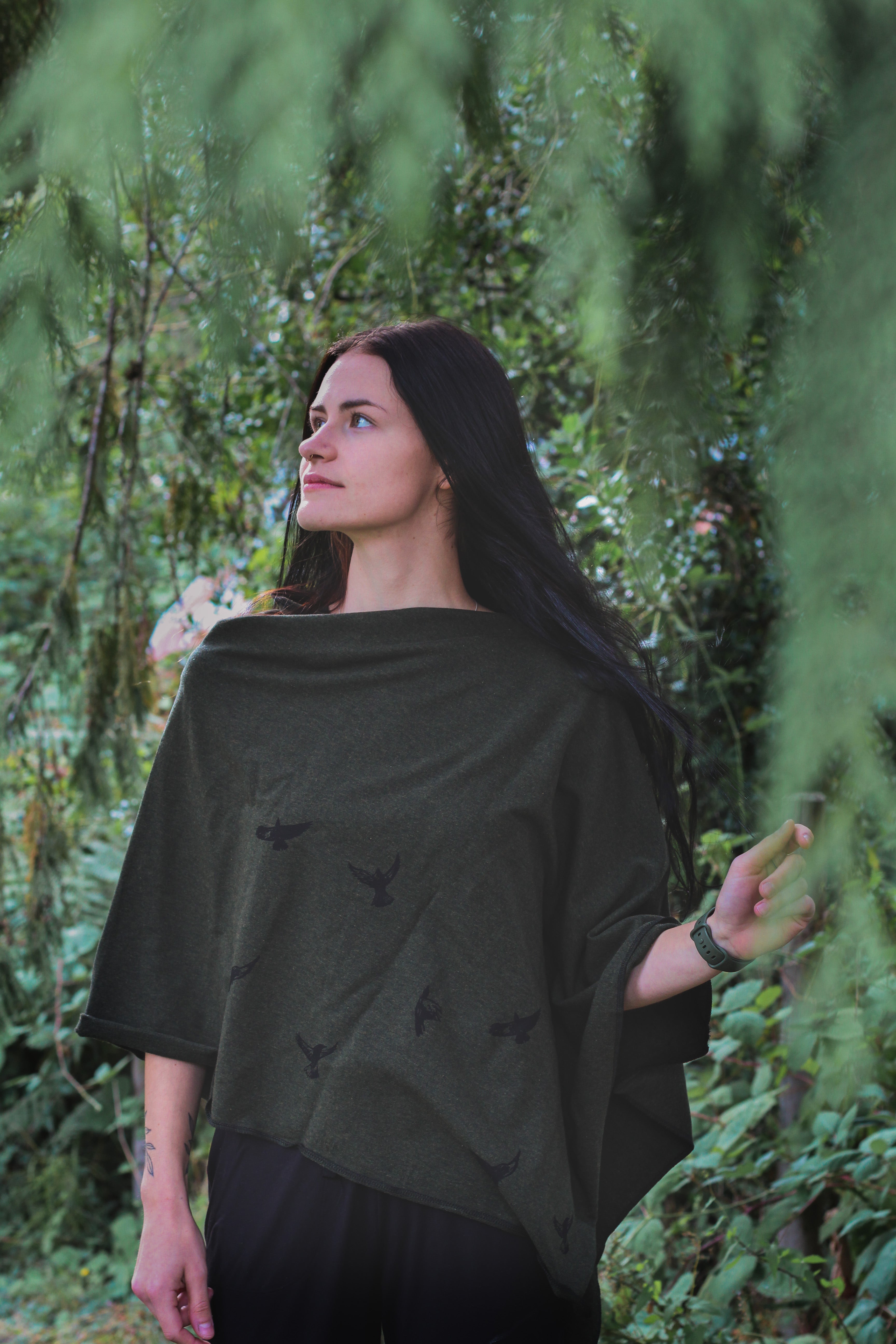 Woman wearing a dark green poncho with butterfly patterns in a forest setting