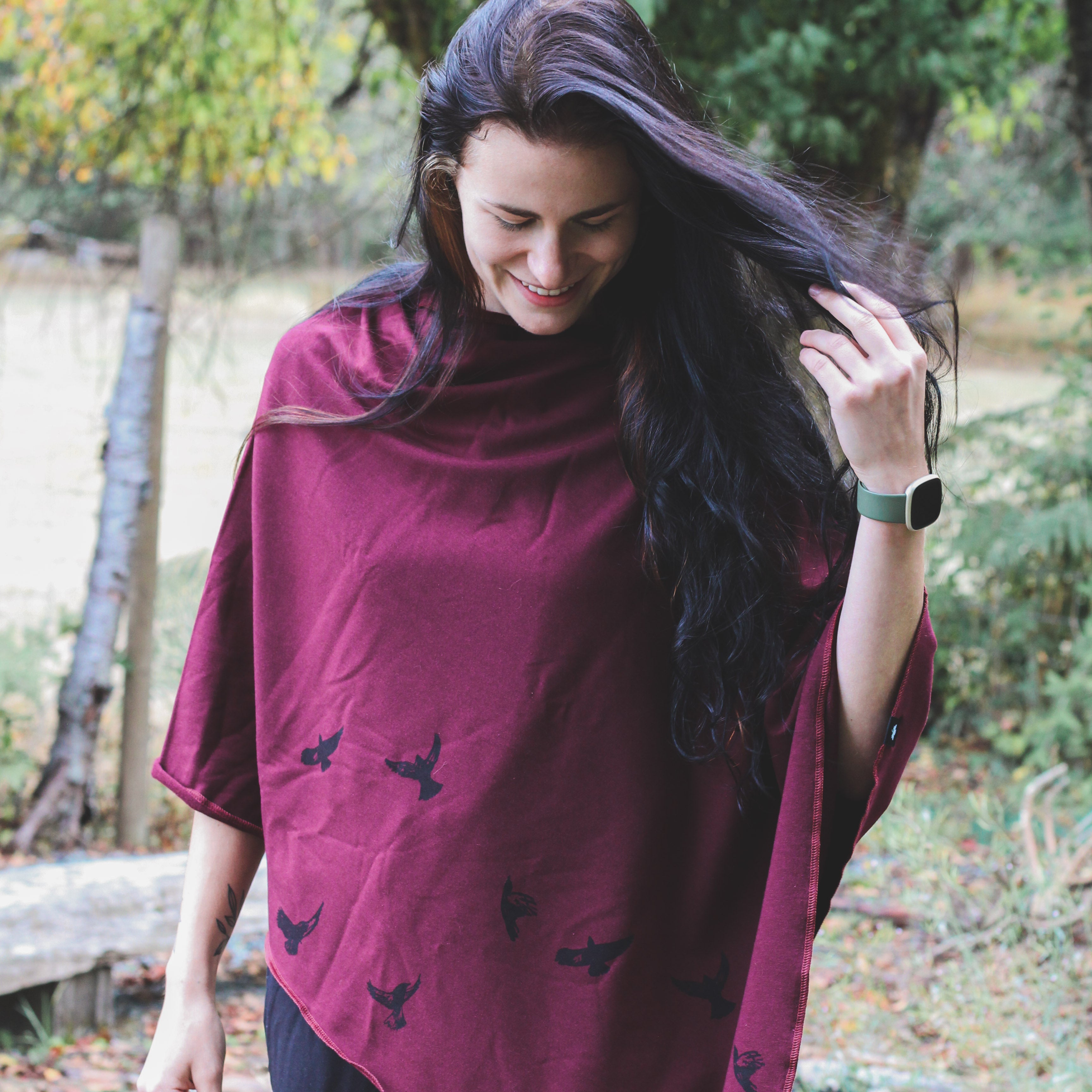 Woman wearing a burgundy poncho with black bird patterns in an outdoor setting.